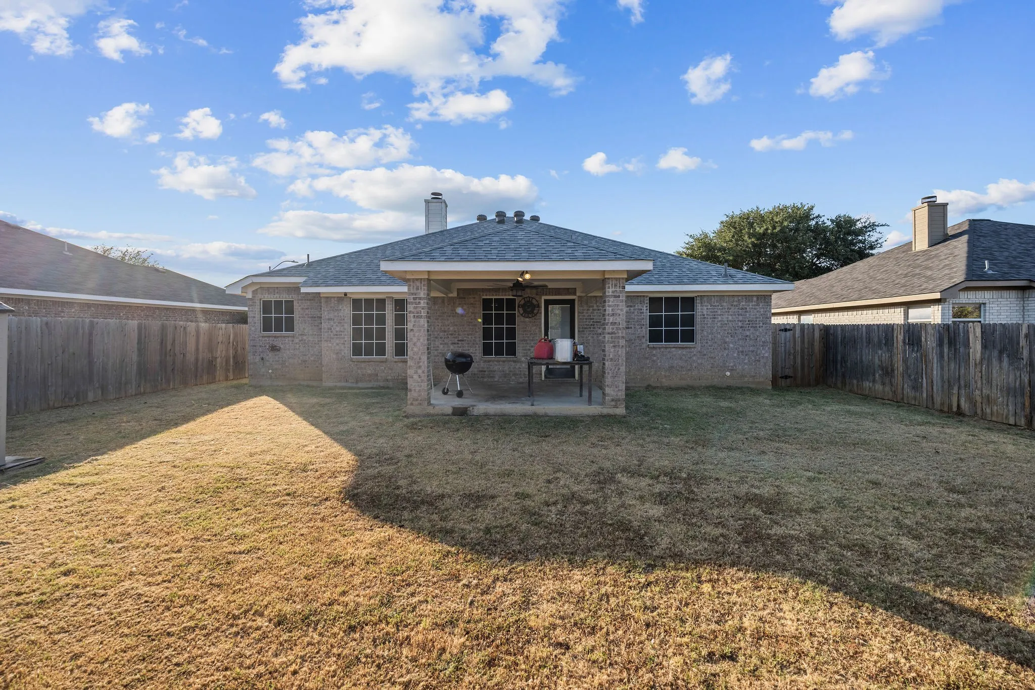 Expansive backyard featuring a covered patio with a ceiling fan, brick exterior, fenced perimeter, and a shingled roof