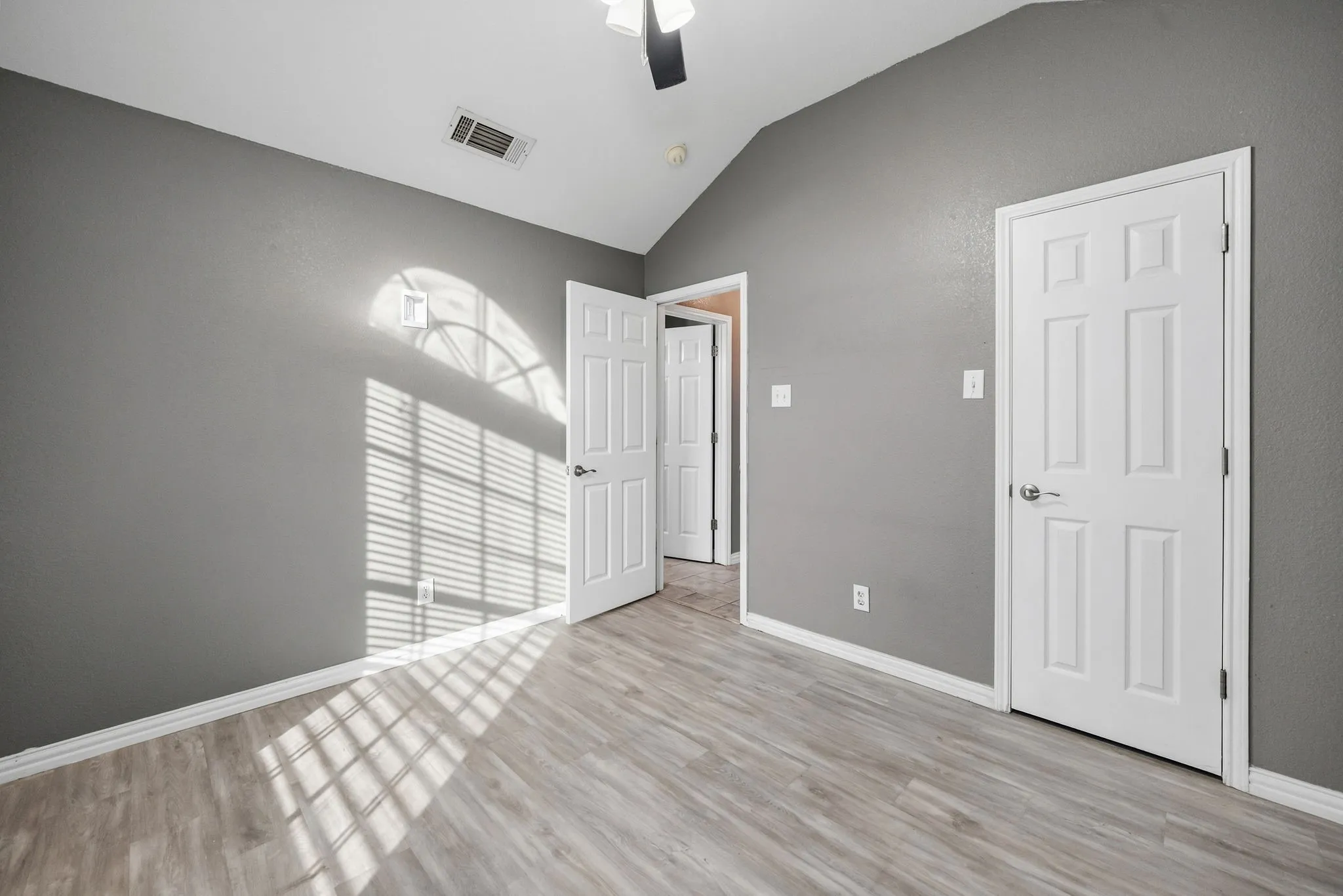Vaulted ceiling with a ceiling fan, wood-finish flooring, and white paneled doors