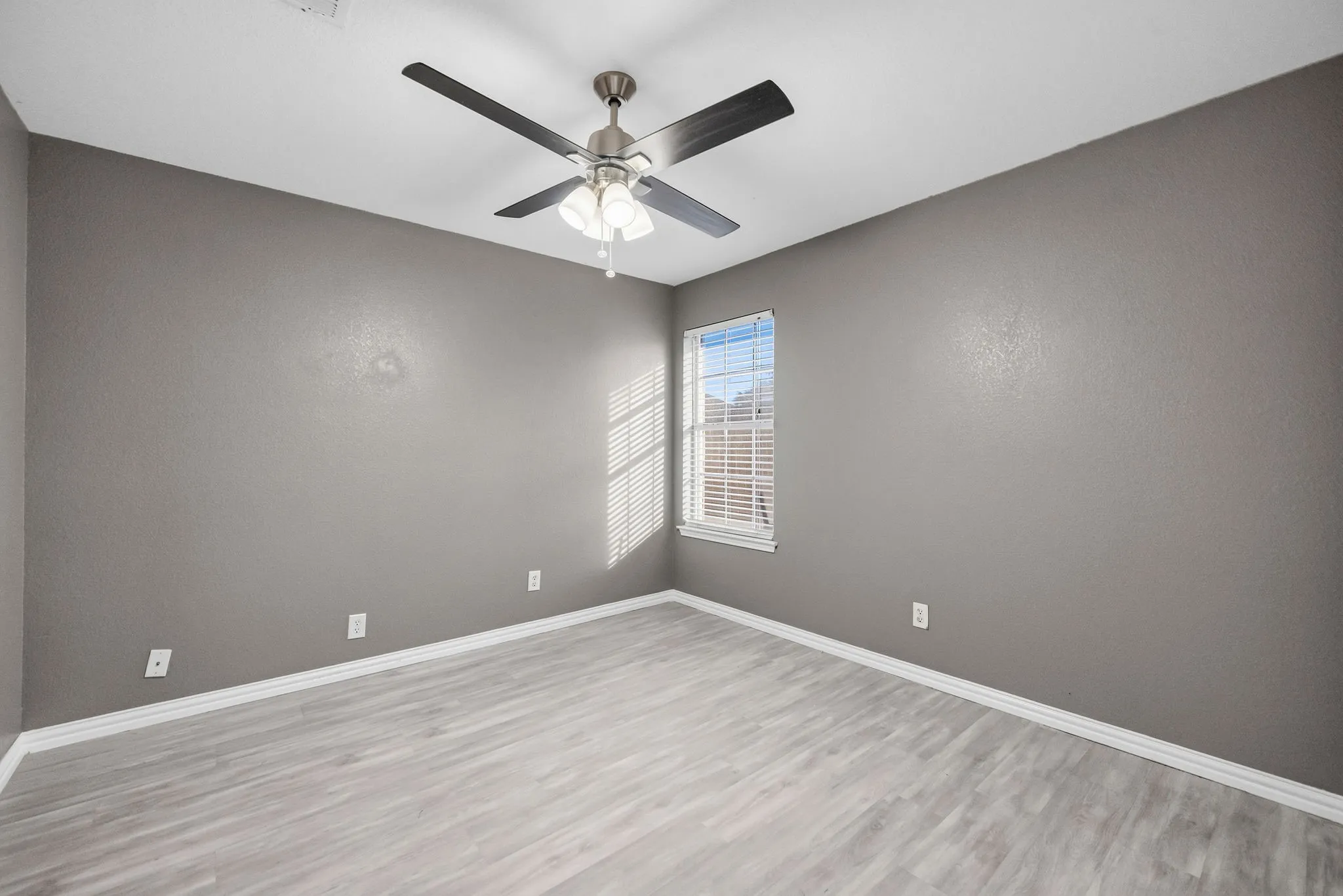 Wood-finish flooring, ceiling fan with light fixture, single window with blinds, and neutral wall tones
