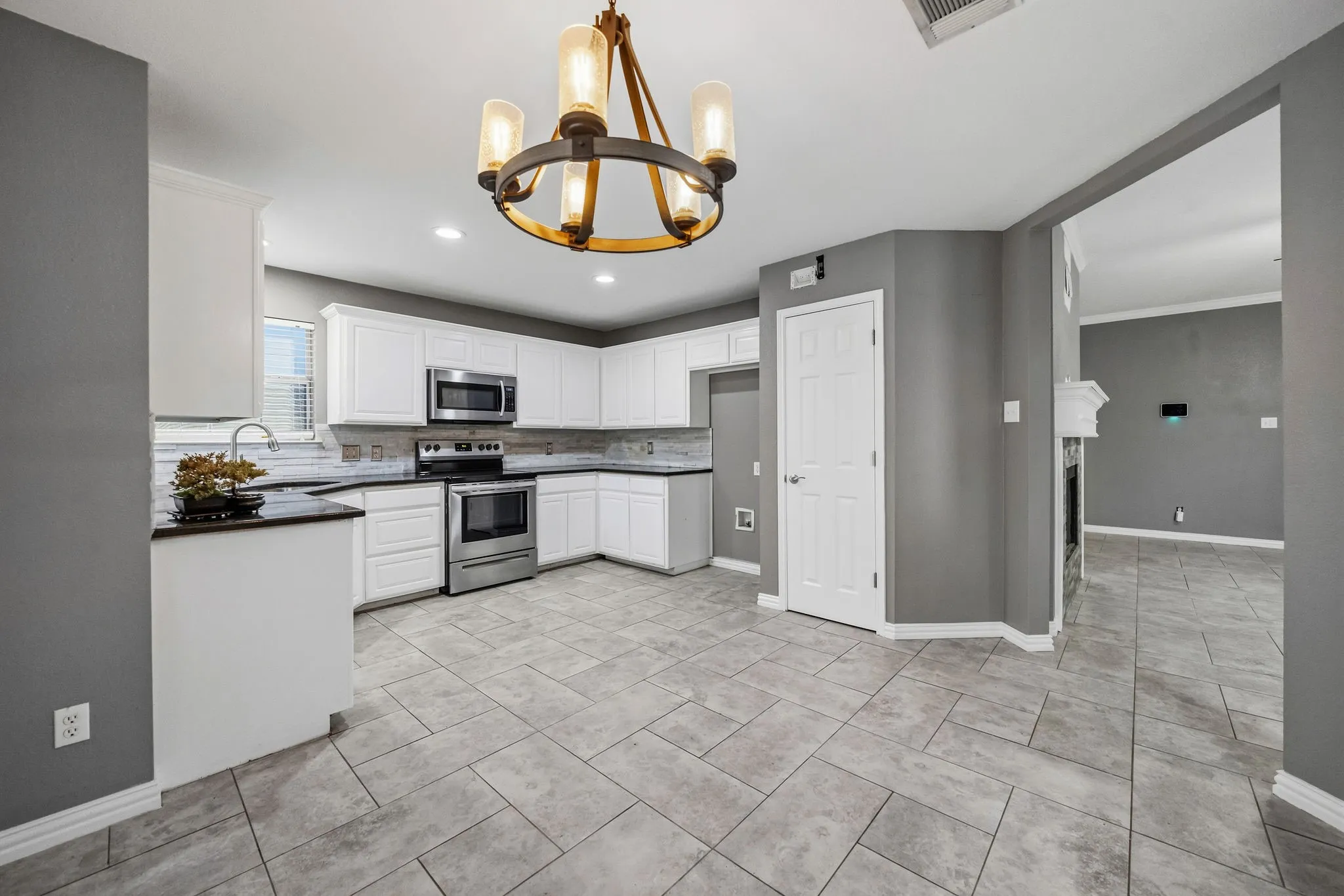 Kitchen featuring white cabinetry, stainless steel appliances, dark countertops, and gray tile flooring