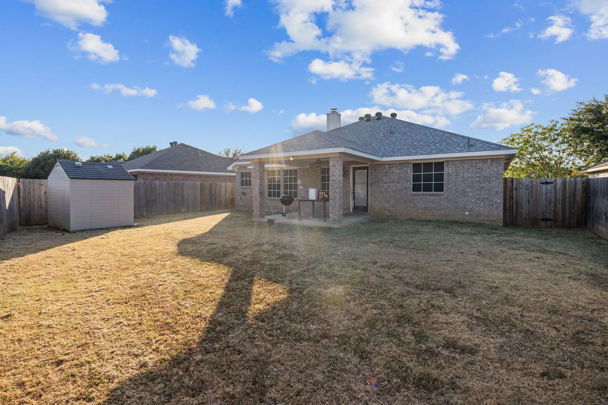 Expansive backyard with a covered patio, full brick exterior, privacy fencing, and a separate storage shed
