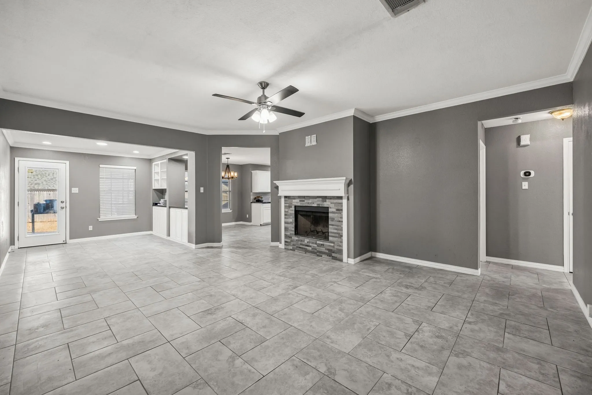 Spacious living area featuring tile flooring, a fireplace with a stone surround and mantel, and an overhead ceiling fan