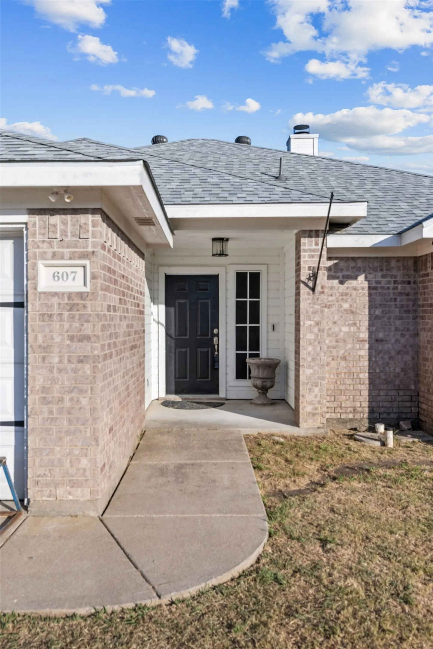 Brick facade home featuring a prominent dark entry door, a covered front porch, and a concrete pathway