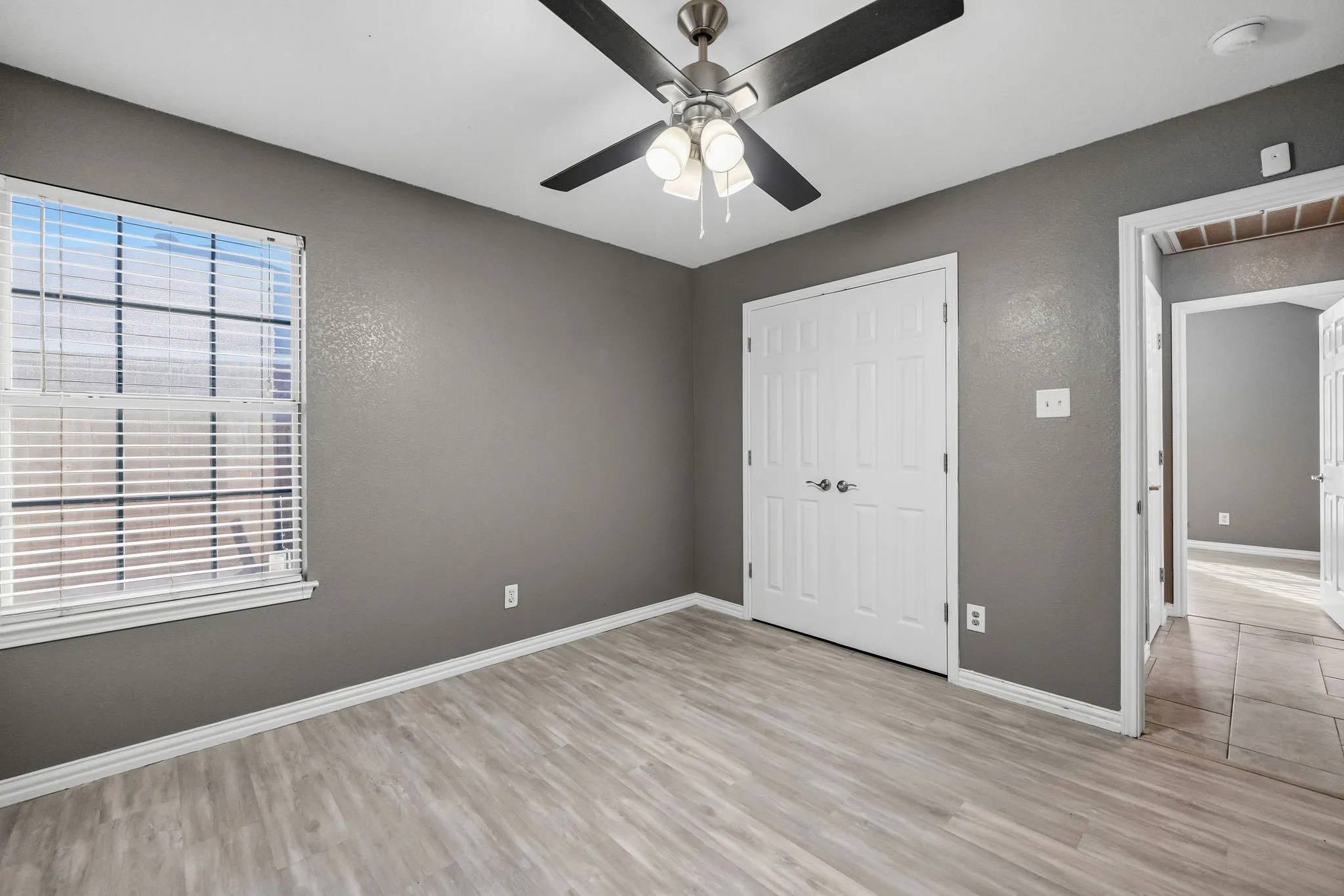 Room featuring wood-finish flooring, a ceiling fan with light, a window with blinds, and white bi-fold closet doors