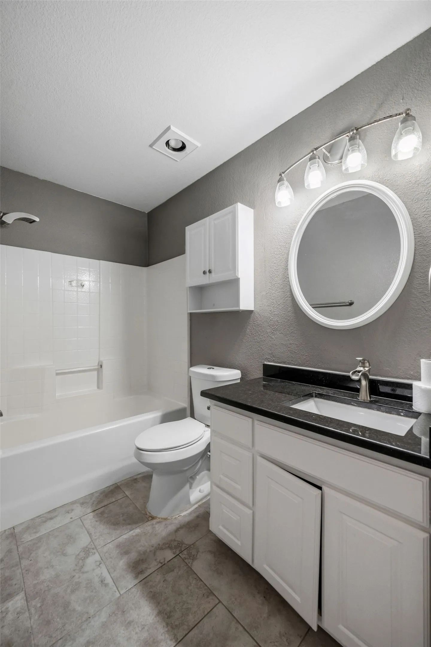 White vanity with a dark countertop, an undermount sink, and a framed mirror