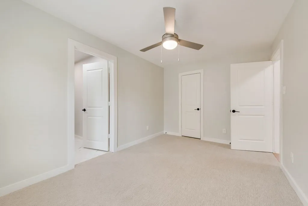 Neutral-toned carpeting, modern ceiling fan, white interior doors, and crisp white trim