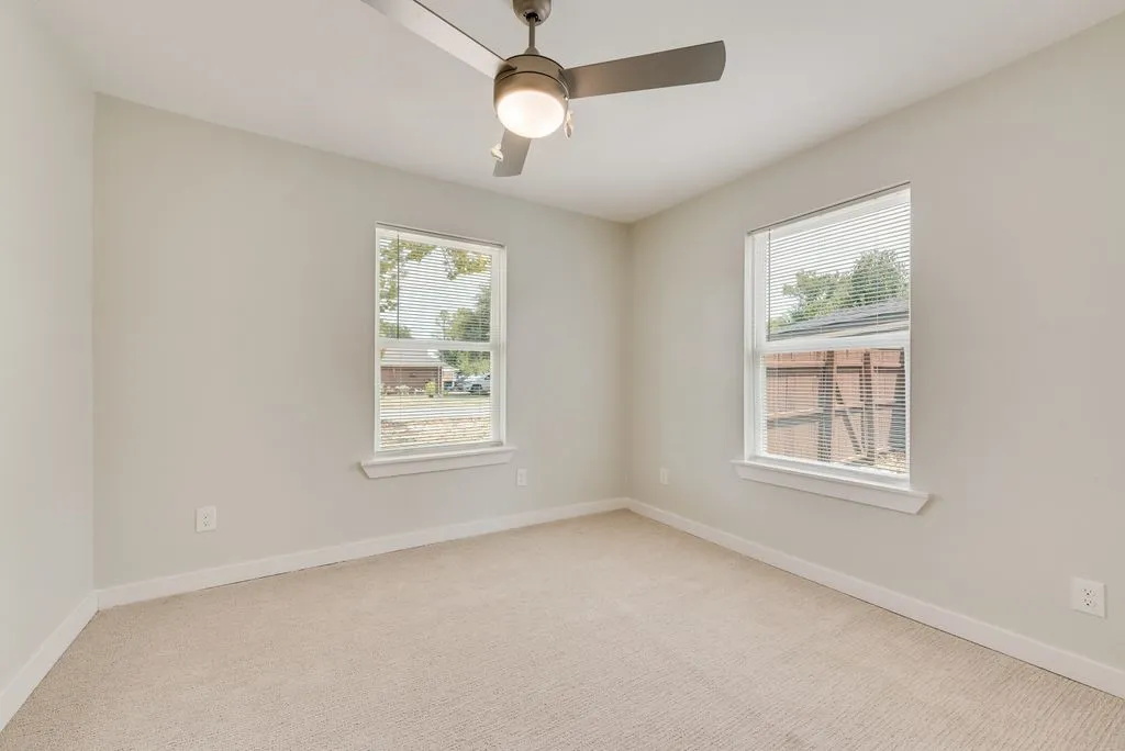 Neutral wall finishes, dual window placements, ceiling fan with integrated lighting, and carpeted flooring