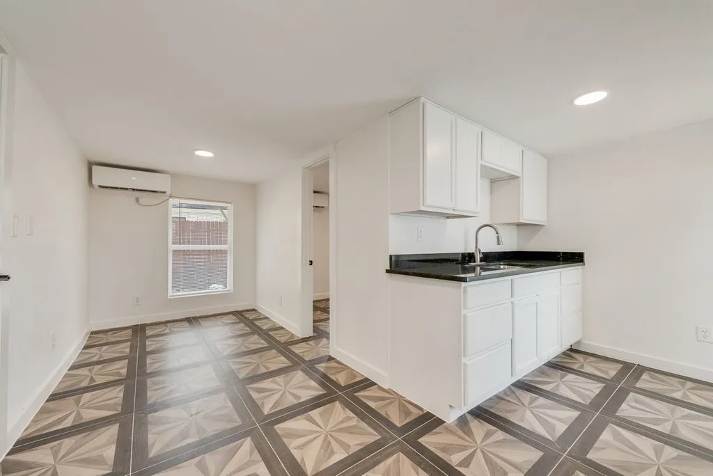Guest Quarters Compact kitchen area with white cabinetry, dark countertops, and a stainless steel sink