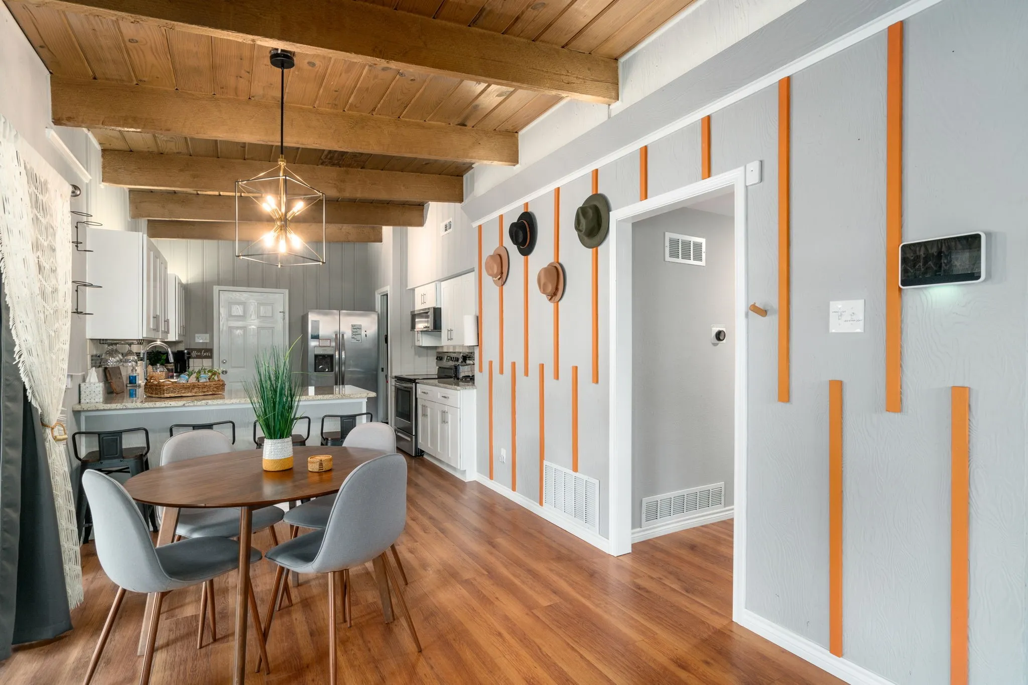 Vaulted wood-beamed ceiling, wood-finish flooring, white cabinetry, integrated kitchen appliances, and a geometric chandelier