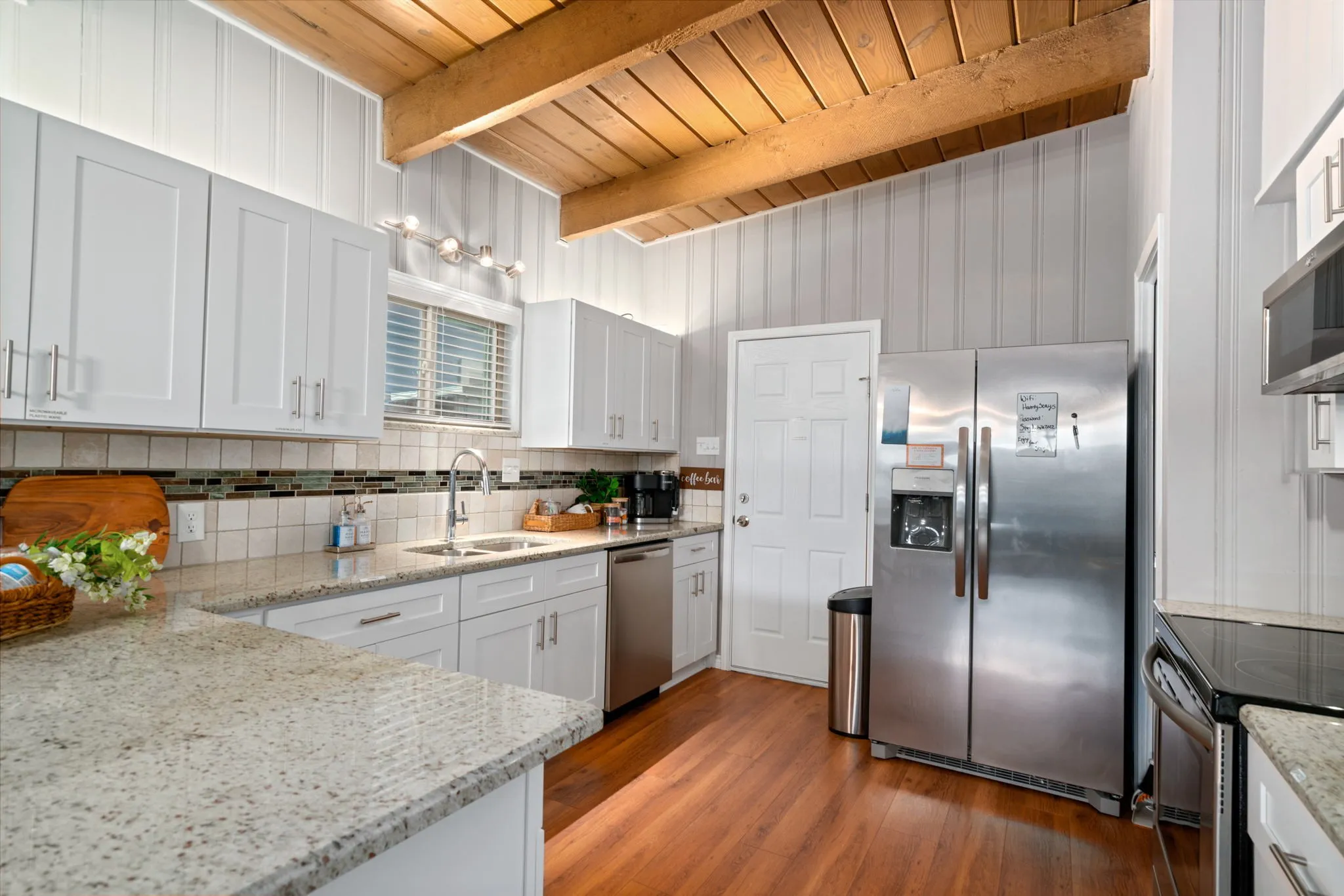 Kitchen featuring wood-finish flooring, white cabinetry, integrated stainless steel appliances, and a tile backsplash