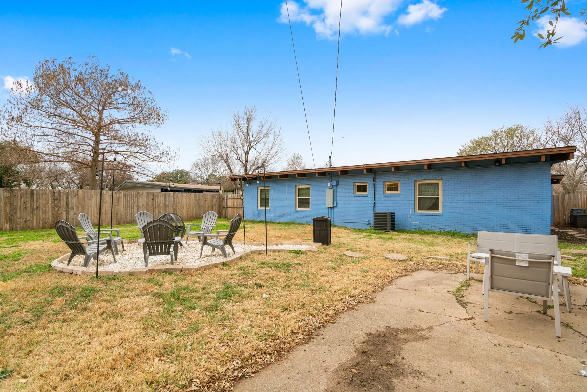 Rear exterior featuring blue brick, multiple windows, an air conditioning unit, and a concrete patio area