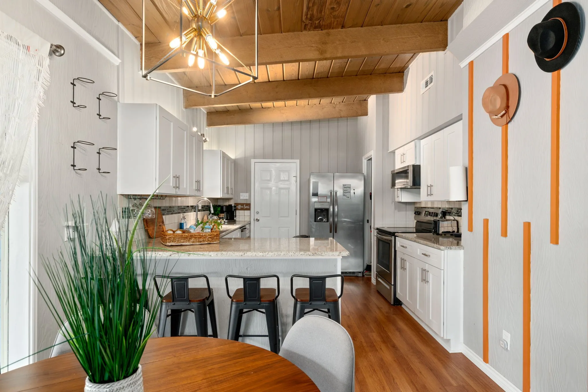 Vaulted wood-plank ceiling with exposed beams, white cabinetry, stainless steel appliances, breakfast bar, and wood-finish flooring