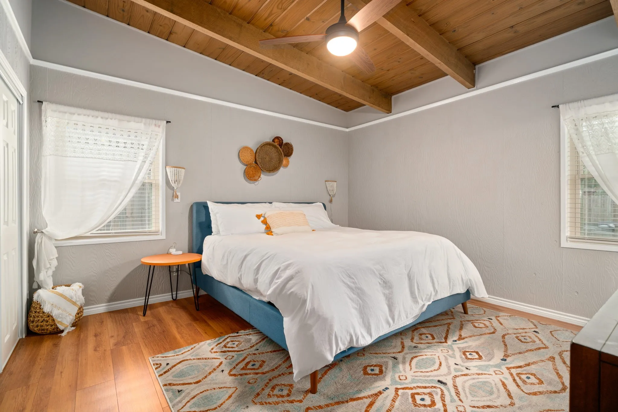 Wood-finish flooring with a ceiling fan, exposed wood beams, and multiple windows
