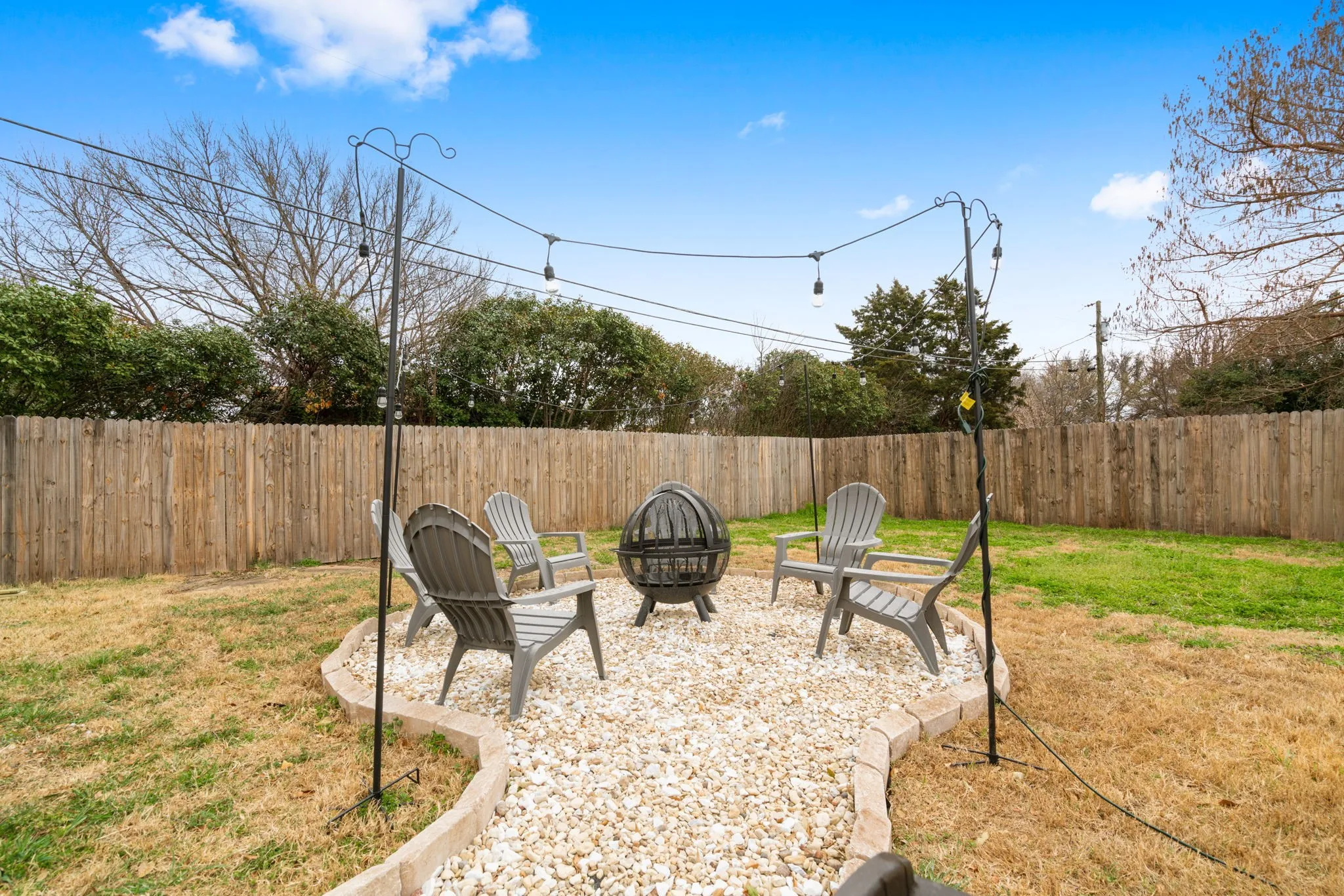 Backyard featuring a privacy fence, gravel patio area, fire pit, and string lighting