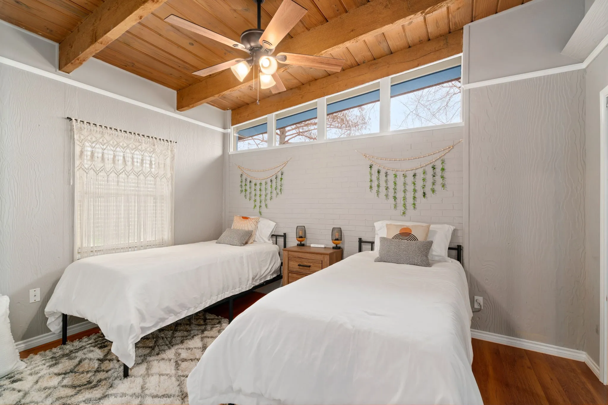 Wood-beamed ceiling with a ceiling fan, clerestory windows, white textured paneling, and wood-finish flooring