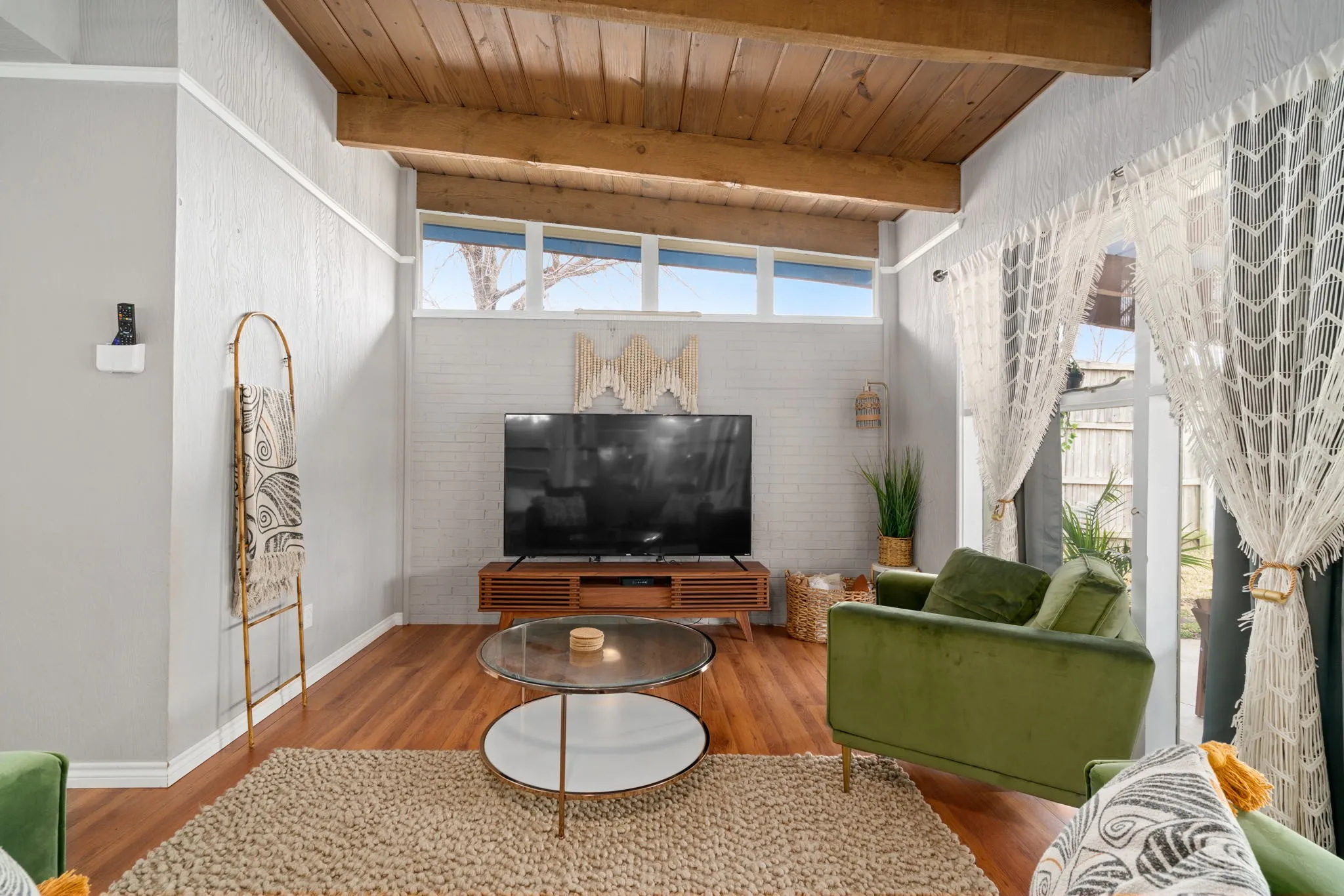 Vaulted ceiling with exposed wood beams, clerestory windows, wood-finish flooring, and a white brick-finish accent wall