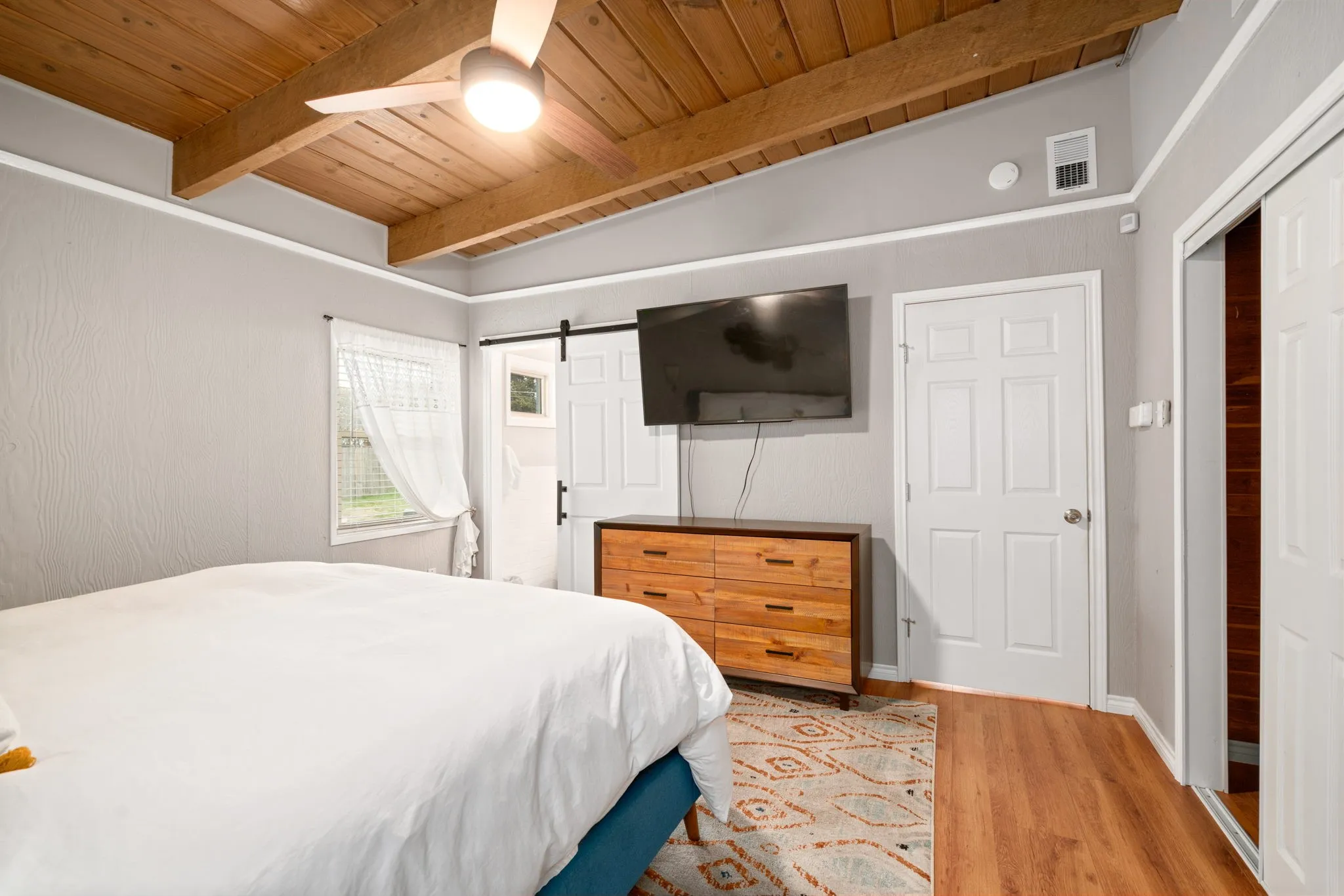 Bright bedroom with wood-finish flooring, wooden ceiling beams, and recessed lighting throughout
