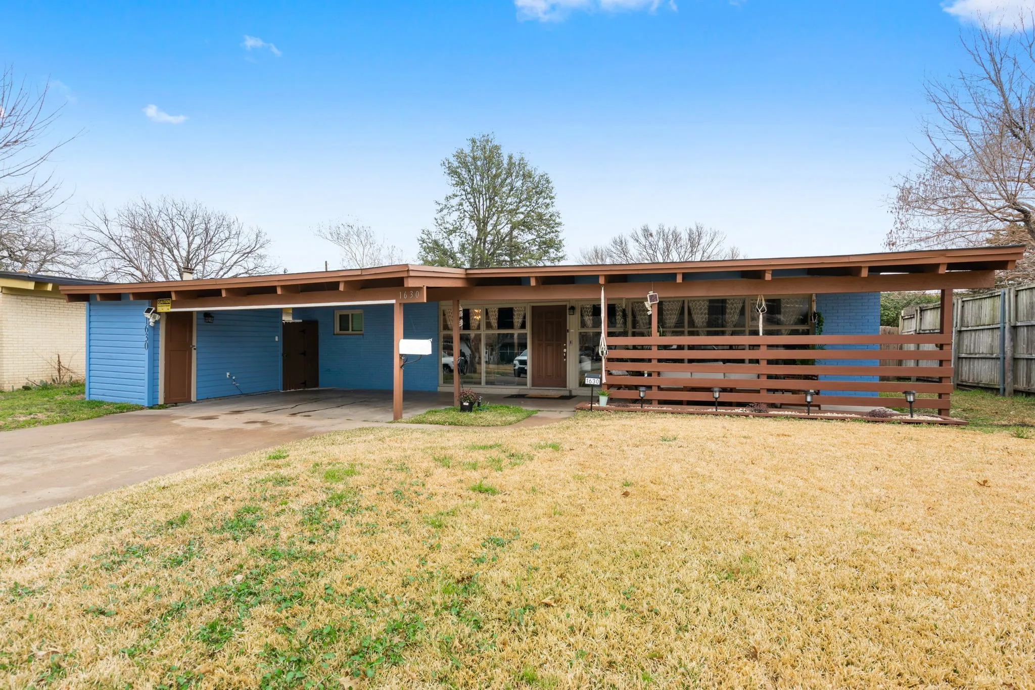 Exterior featuring a carport, horizontal wood-slat fencing, expansive front windows, and a flat roofline