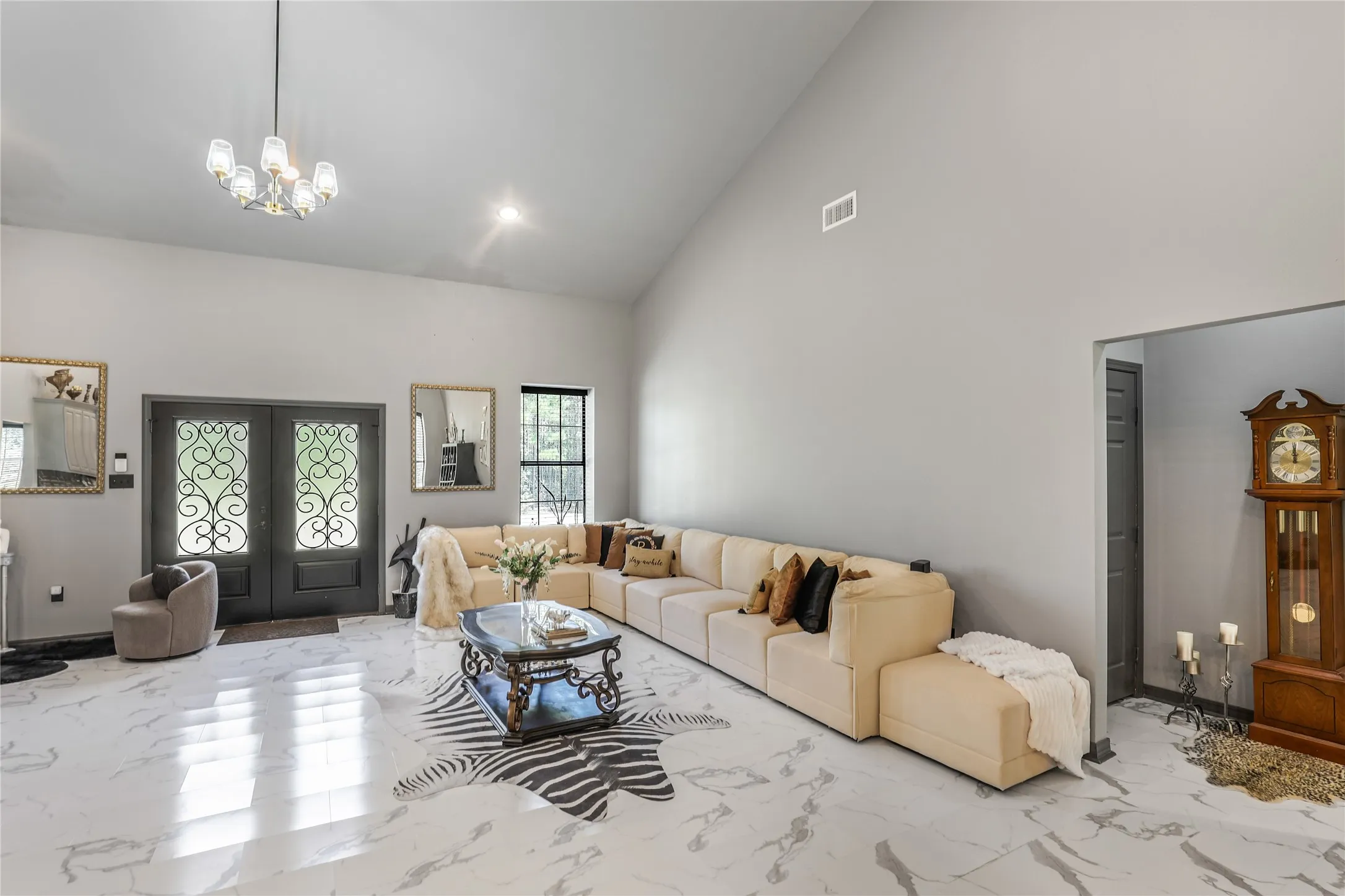 Vaulted ceiling, double entry doors with decorative ironwork, chandelier, large windows, and sleek tile flooring