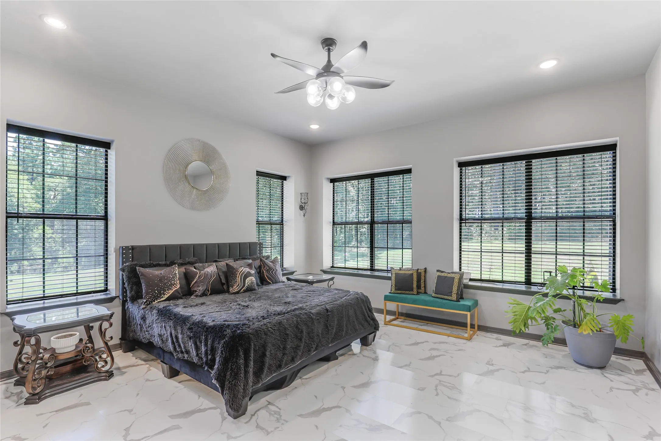 Spacious room featuring light-toned walls, recessed lighting, a ceiling fan with integrated lighting, multiple windows with dark frames, and large format tile flooring