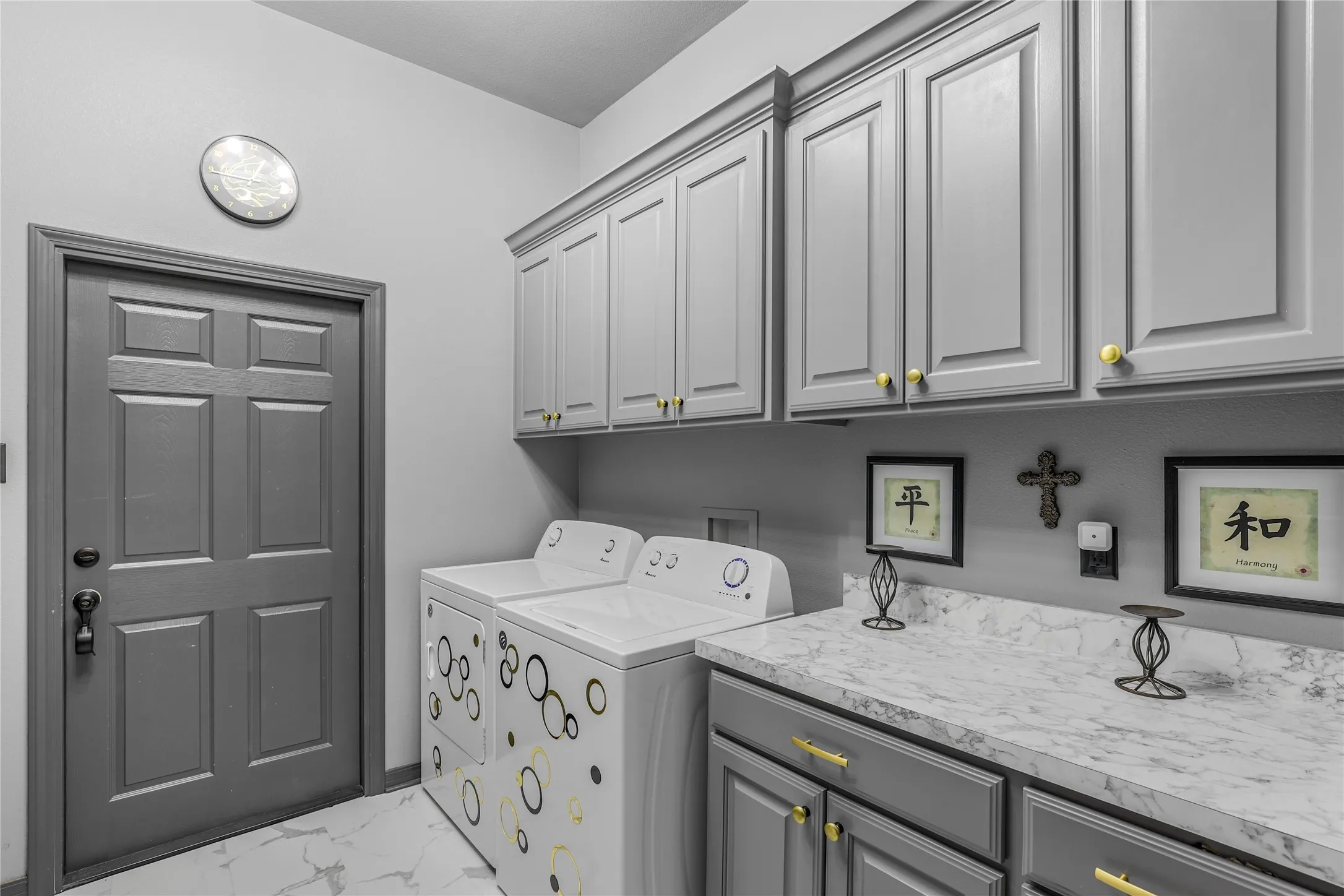Light gray shaker-style cabinetry with gold-tone hardware, white marble-patterned countertop, and white flooring with gray veining