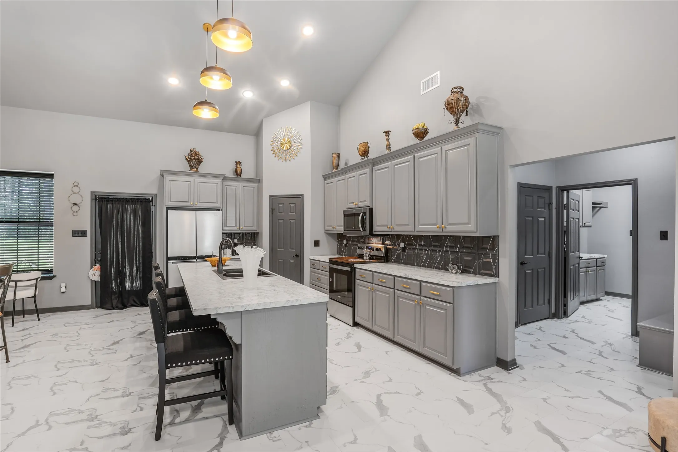 Vaulted ceiling kitchen featuring an island with a breakfast bar, stainless steel appliances, abundant cabinetry, and patterned tile flooring