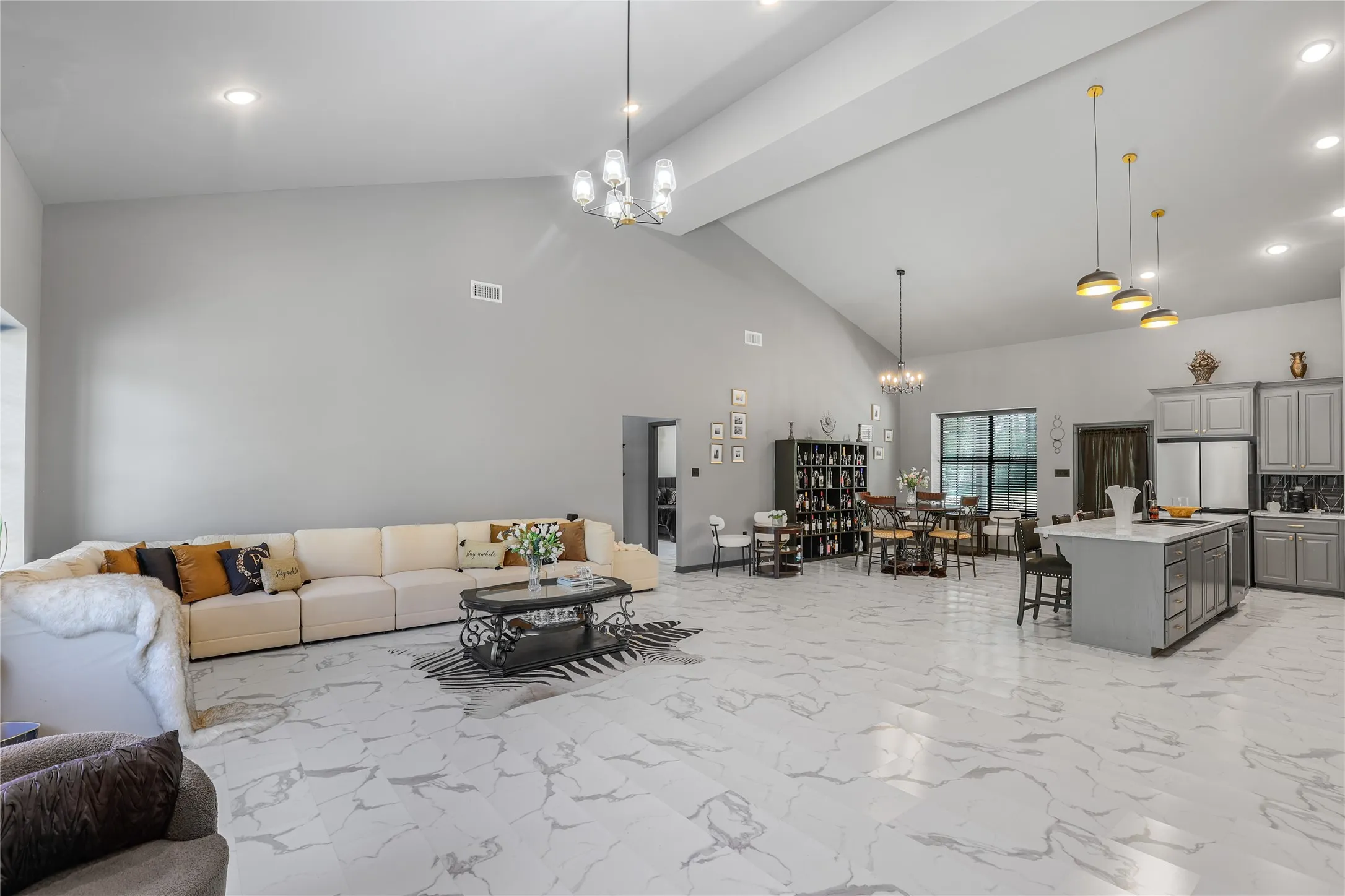 Spacious open-concept interior featuring vaulted ceilings, large format marble-look flooring, recessed lighting, and a modern kitchen with grey cabinetry and an island