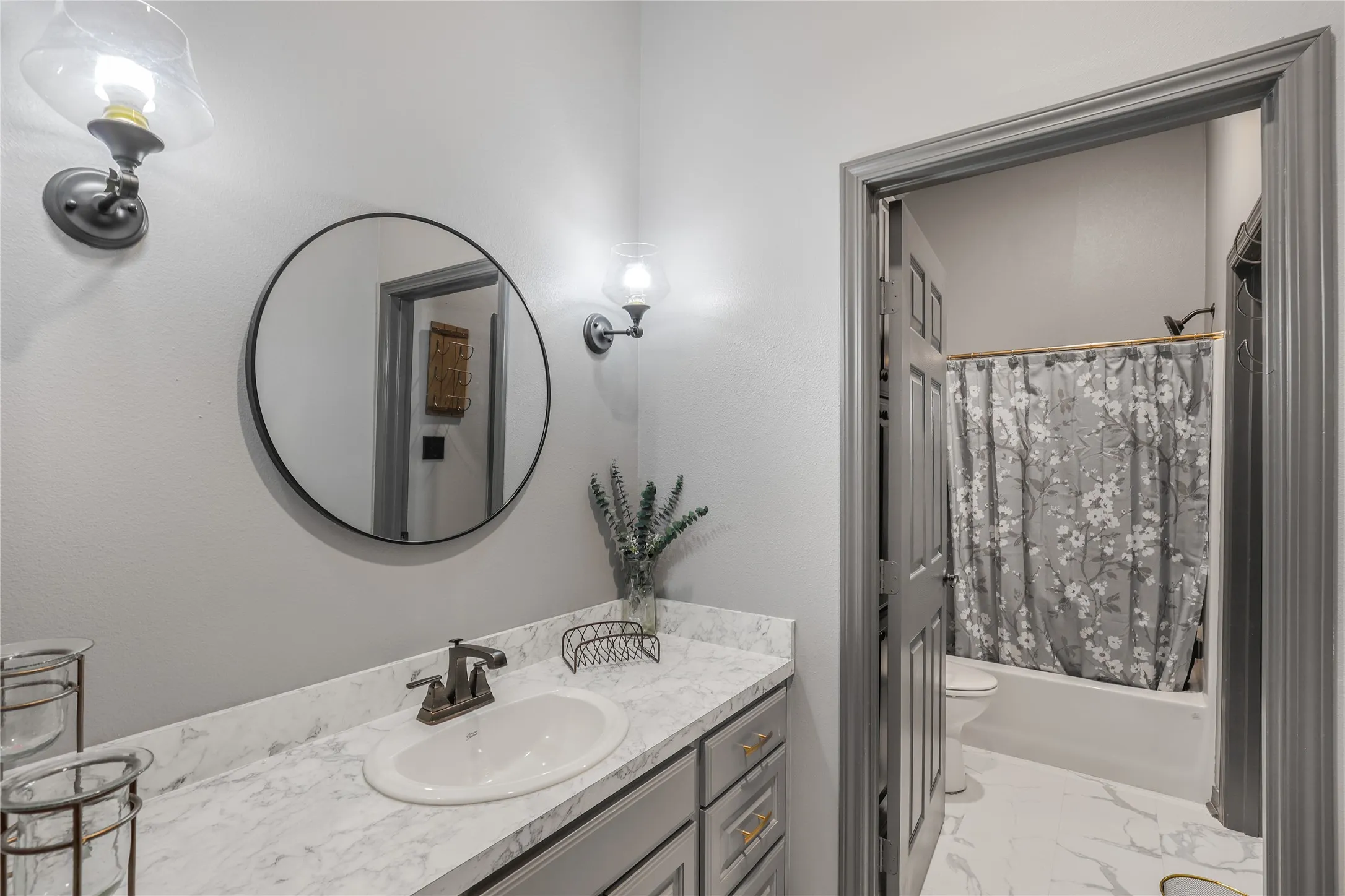 Vanity with a white countertop and integrated sink, framed circular mirror, and adjacent wall sconces