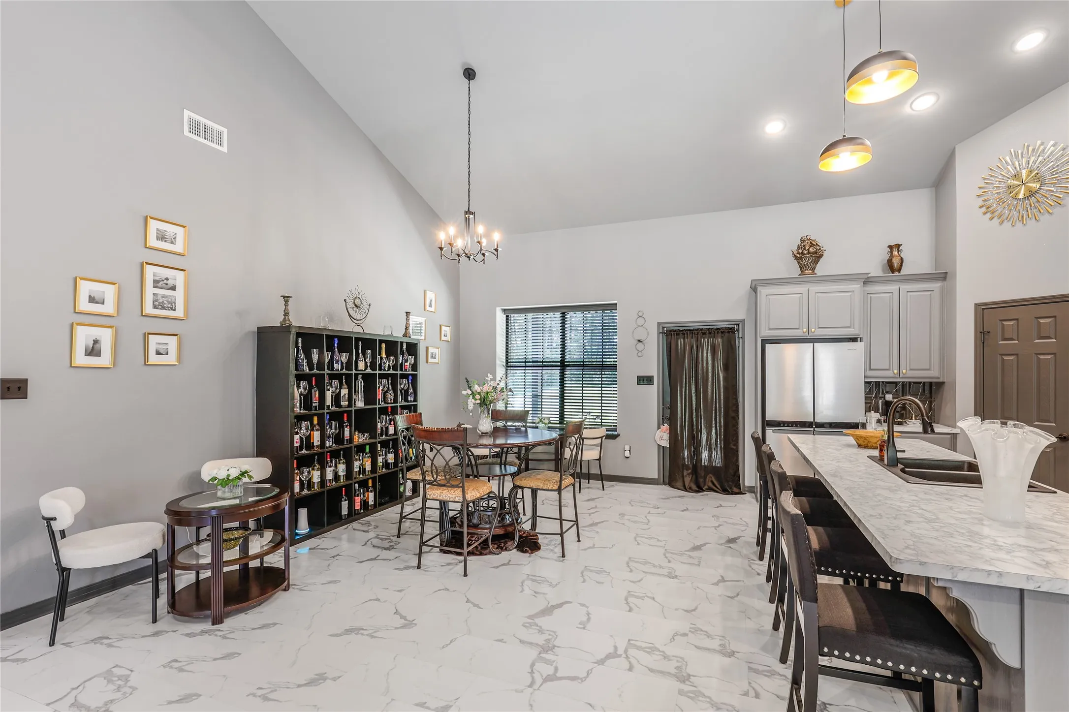 Vaulted ceiling with recessed lighting, large format floor tile, gray cabinetry, stainless steel refrigerator, and breakfast bar