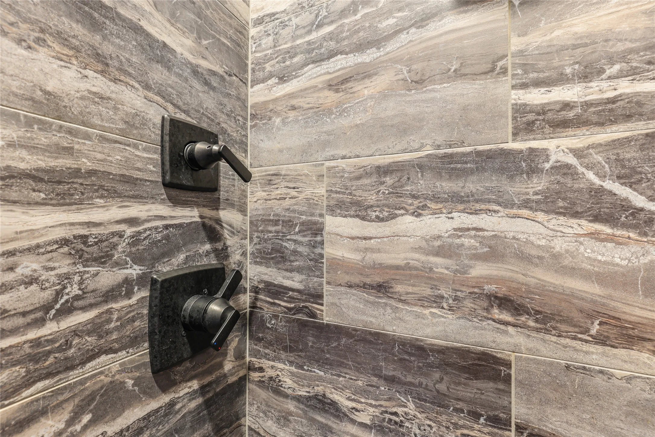Wall-mounted dark bronze shower controls with a tiled shower surround featuring a horizontal linear pattern