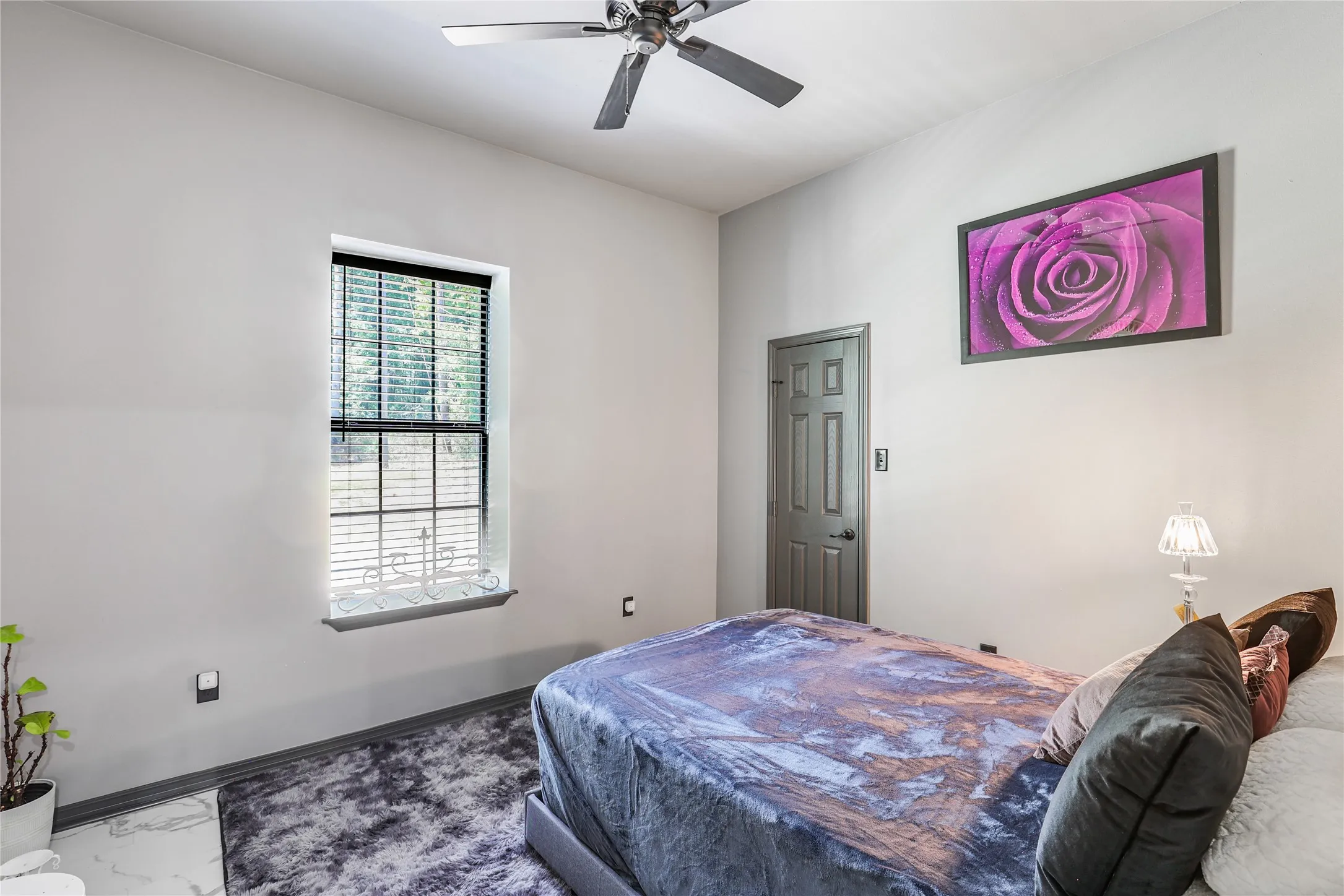 White walls with dark trim, window with blinds, dark paneled door, and a ceiling fan