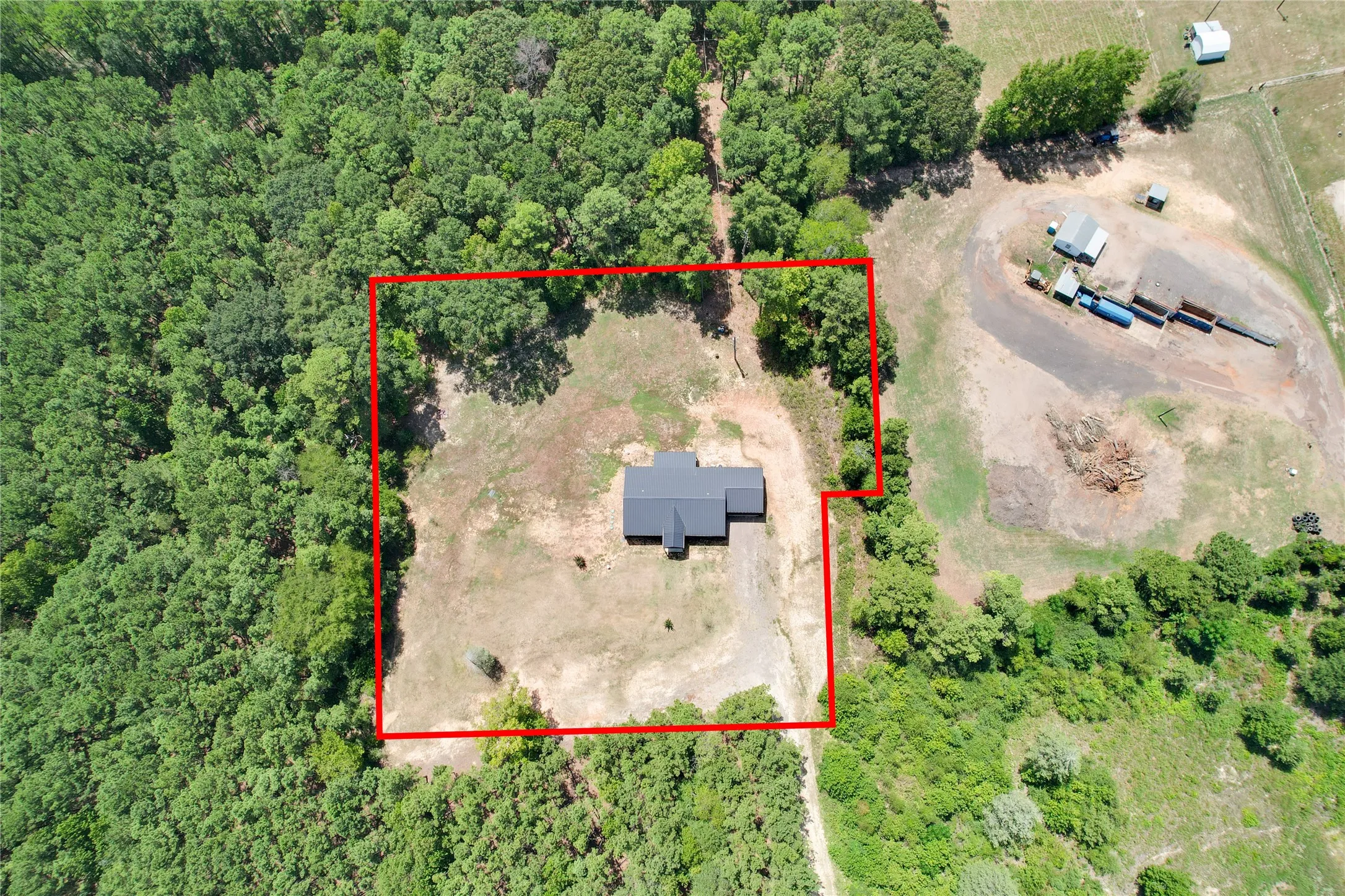 Expansive property featuring a single-story residence with a dark roof, surrounded by mature trees and open land