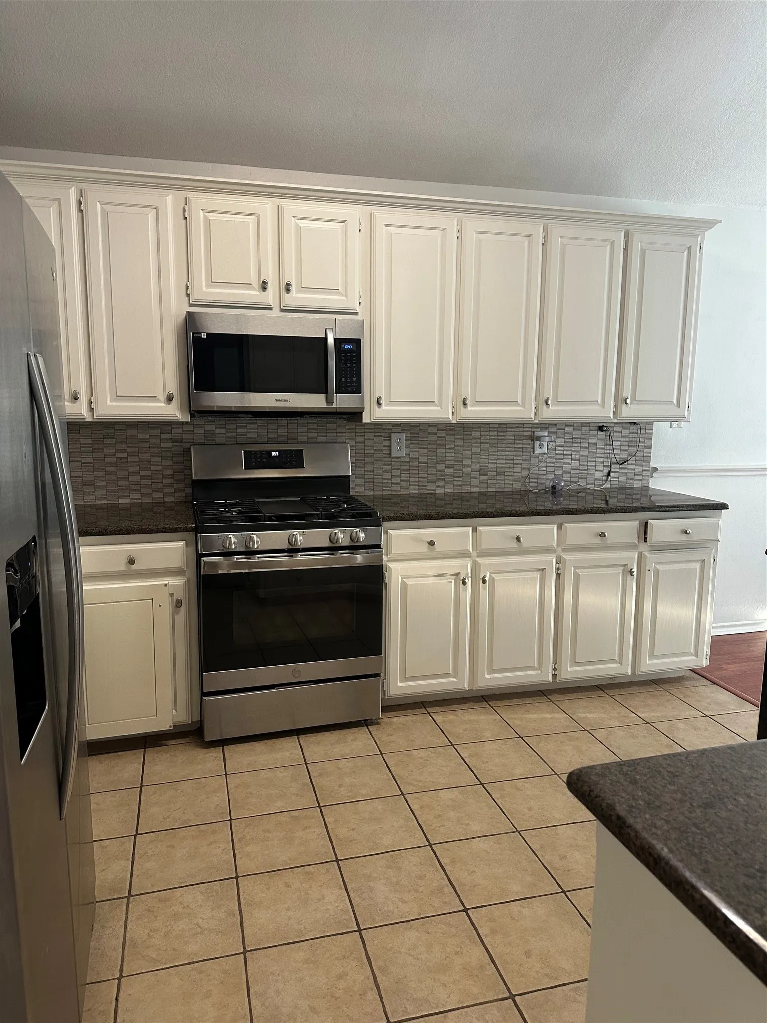 Kitchen featuring white cabinetry, dark countertops, a mosaic tile backsplash, stainless steel appliances, and square tile flooring