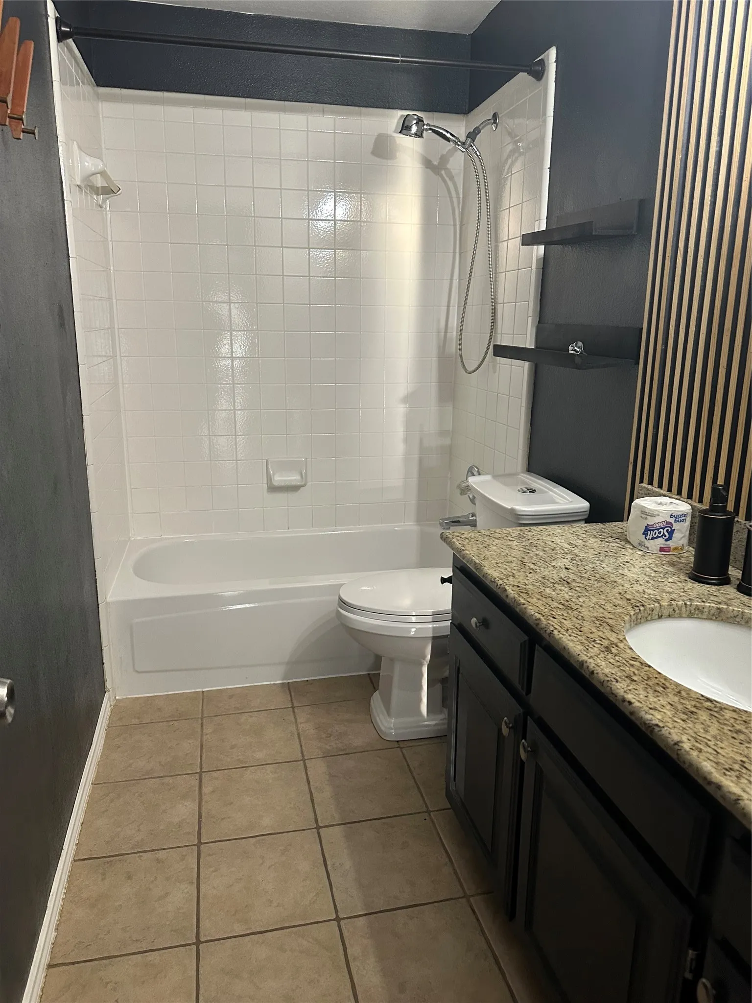 Bathroom featuring a tub/shower combination with white tile surround, ceramic tile flooring, a dark vanity with a light-colored countertop, and a white toilet