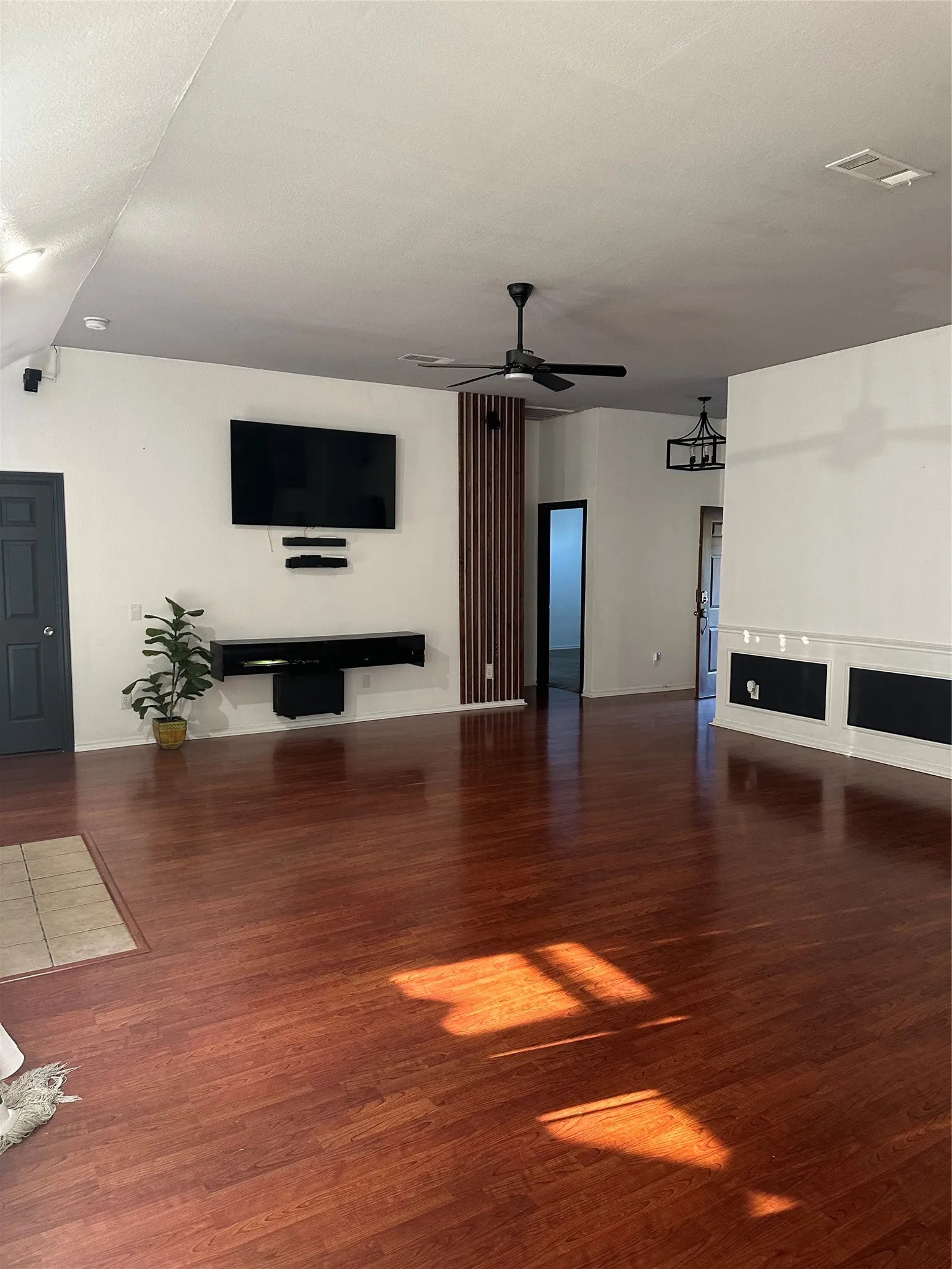 Expansive living space featuring rich wood-finish flooring, a contemporary ceiling fan, and a built-in media console