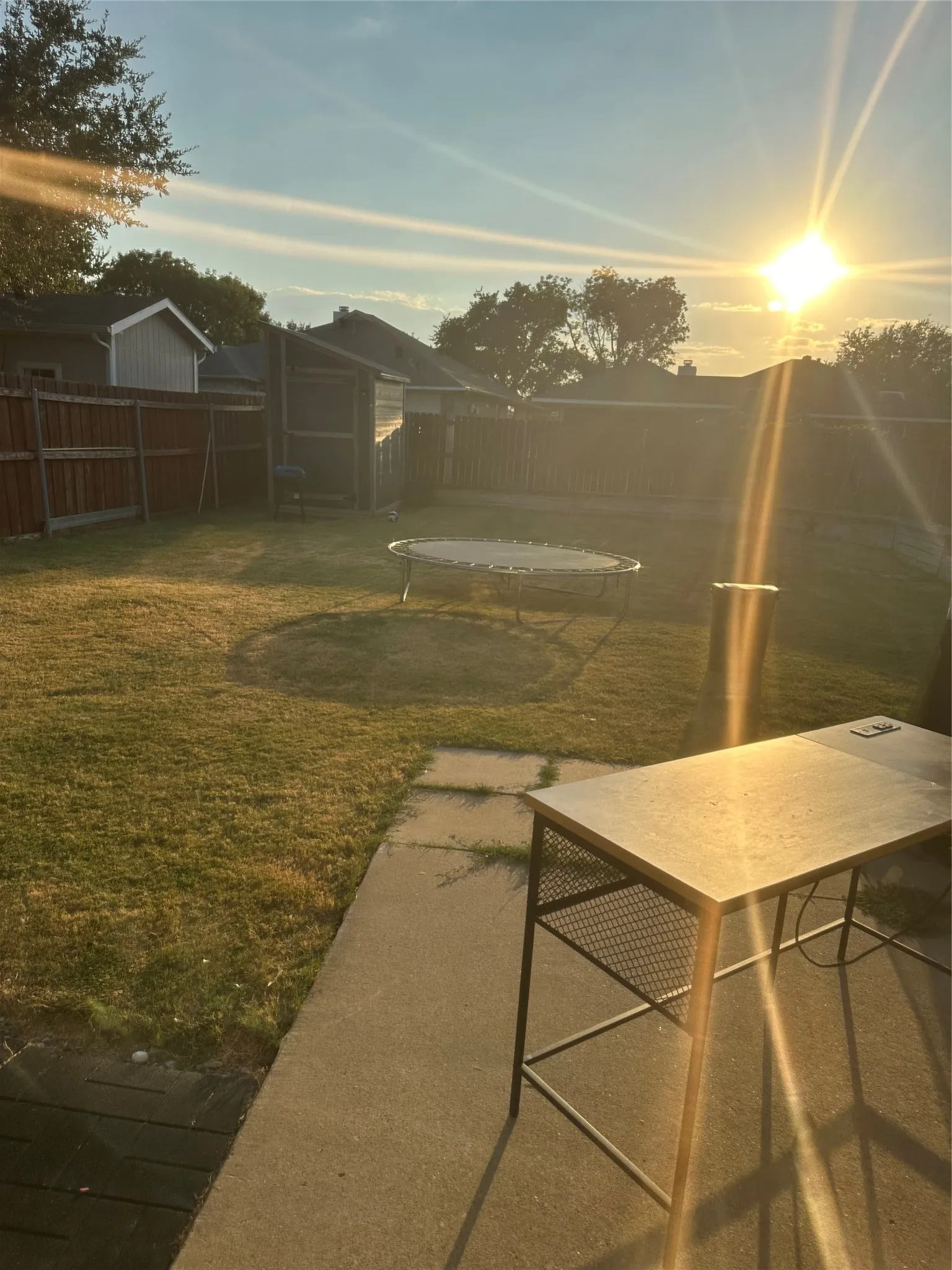 Expansive lawn area with a concrete patio, stepping stones, and wood fencing