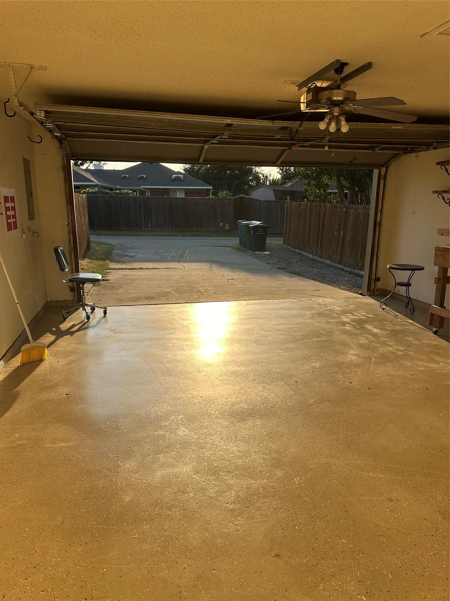 Garage space with concrete flooring, open garage door, and a ceiling fan with integrated lighting