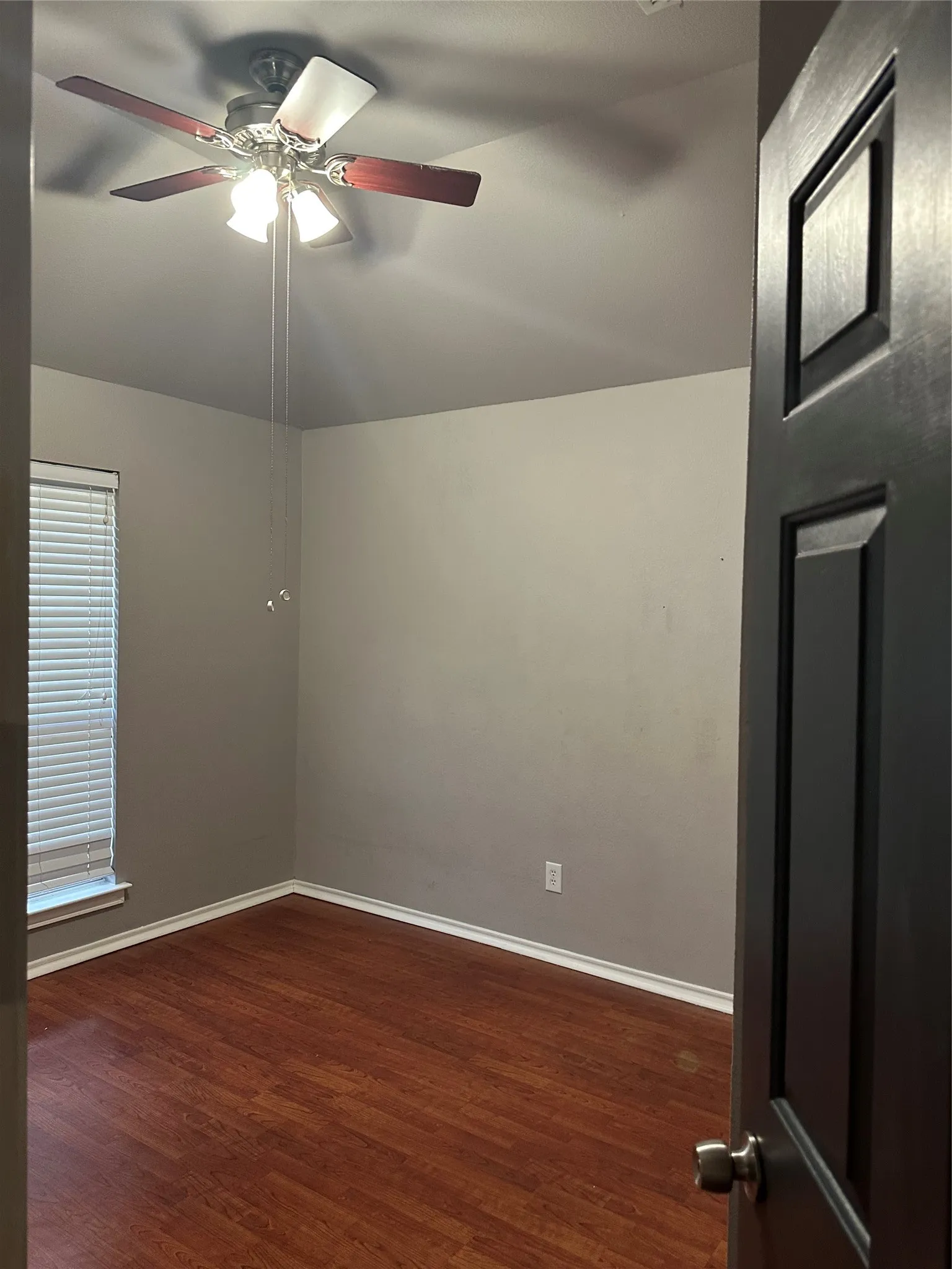 Wood-finish flooring, ceiling fan with integrated lighting, window with horizontal blinds, and a paneled interior door