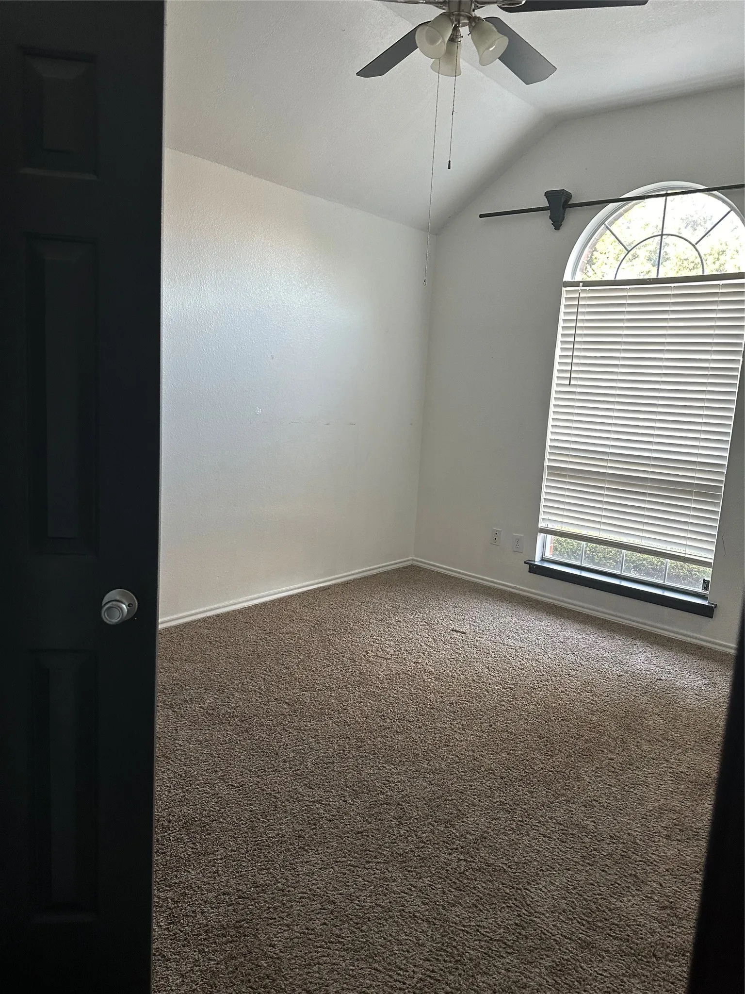 Vaulted ceiling, arched window, ceiling fan with integrated lighting, wall-to-wall carpeting, and white wall finishes