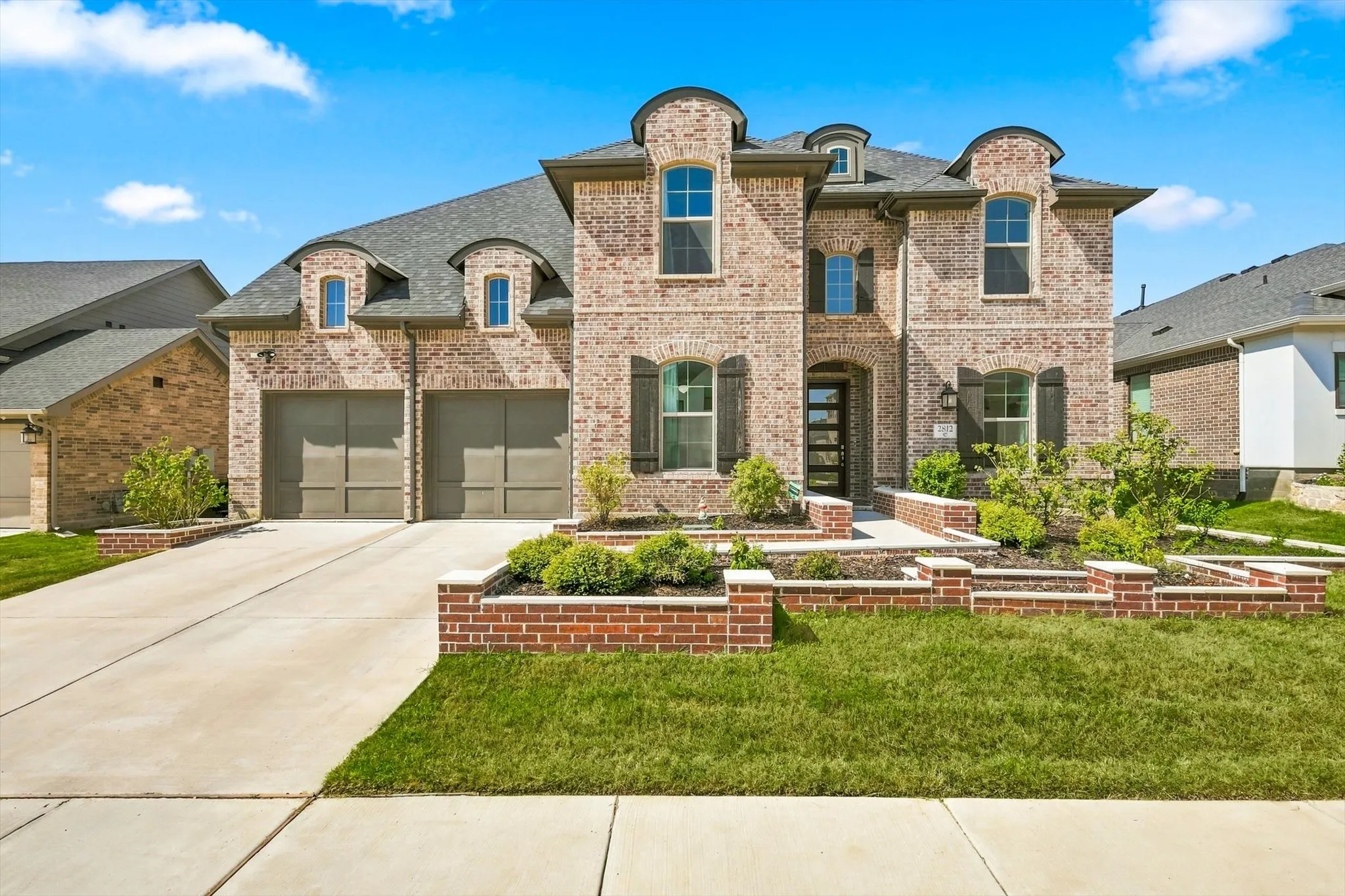 Brick exterior with a multi-gabled roofline, two-car garage, and tiered landscaping beds