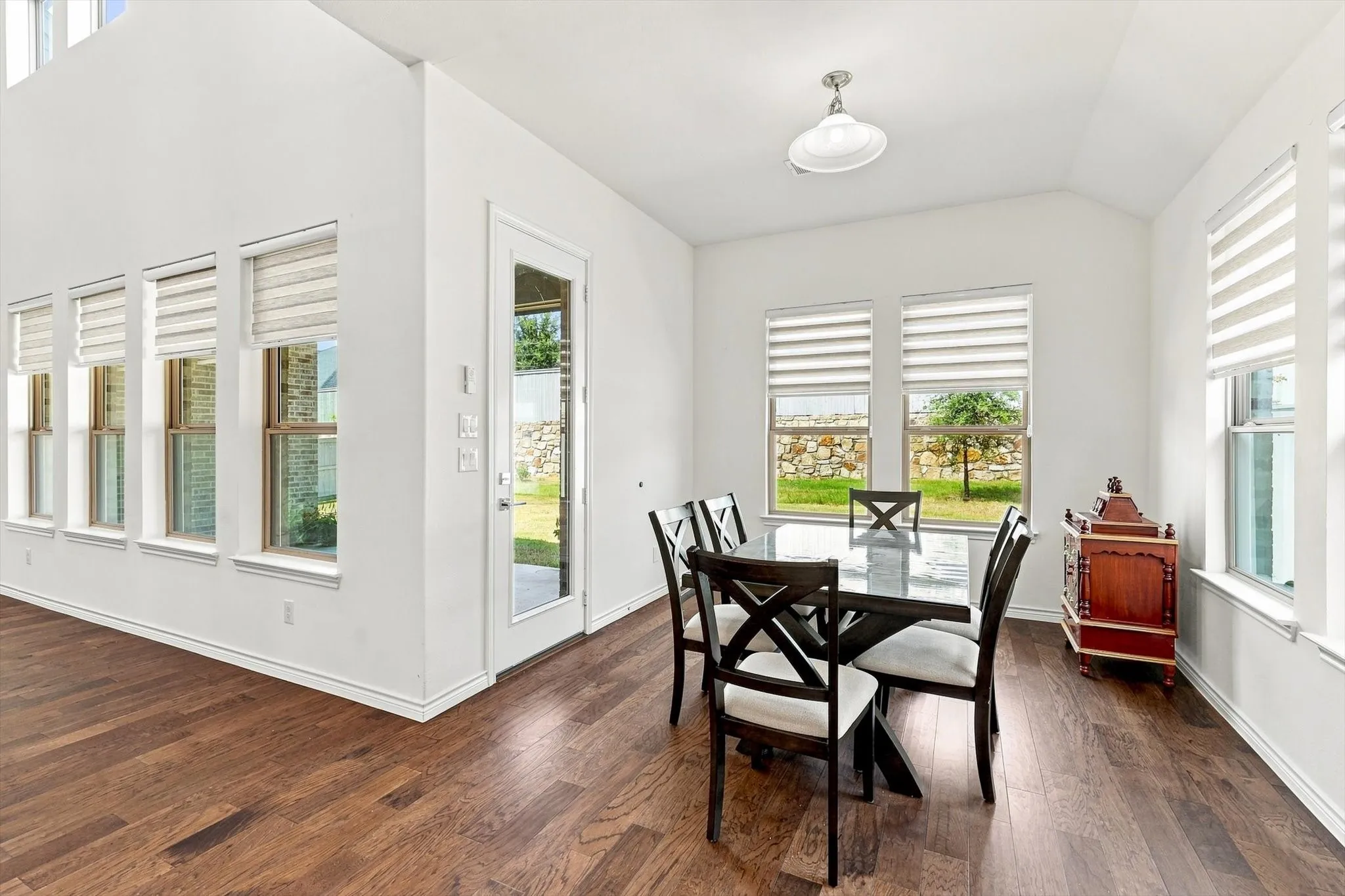 High vaulted ceiling, wood-finish flooring, multiple windows with blinds, recessed lighting, and a glass-paneled door