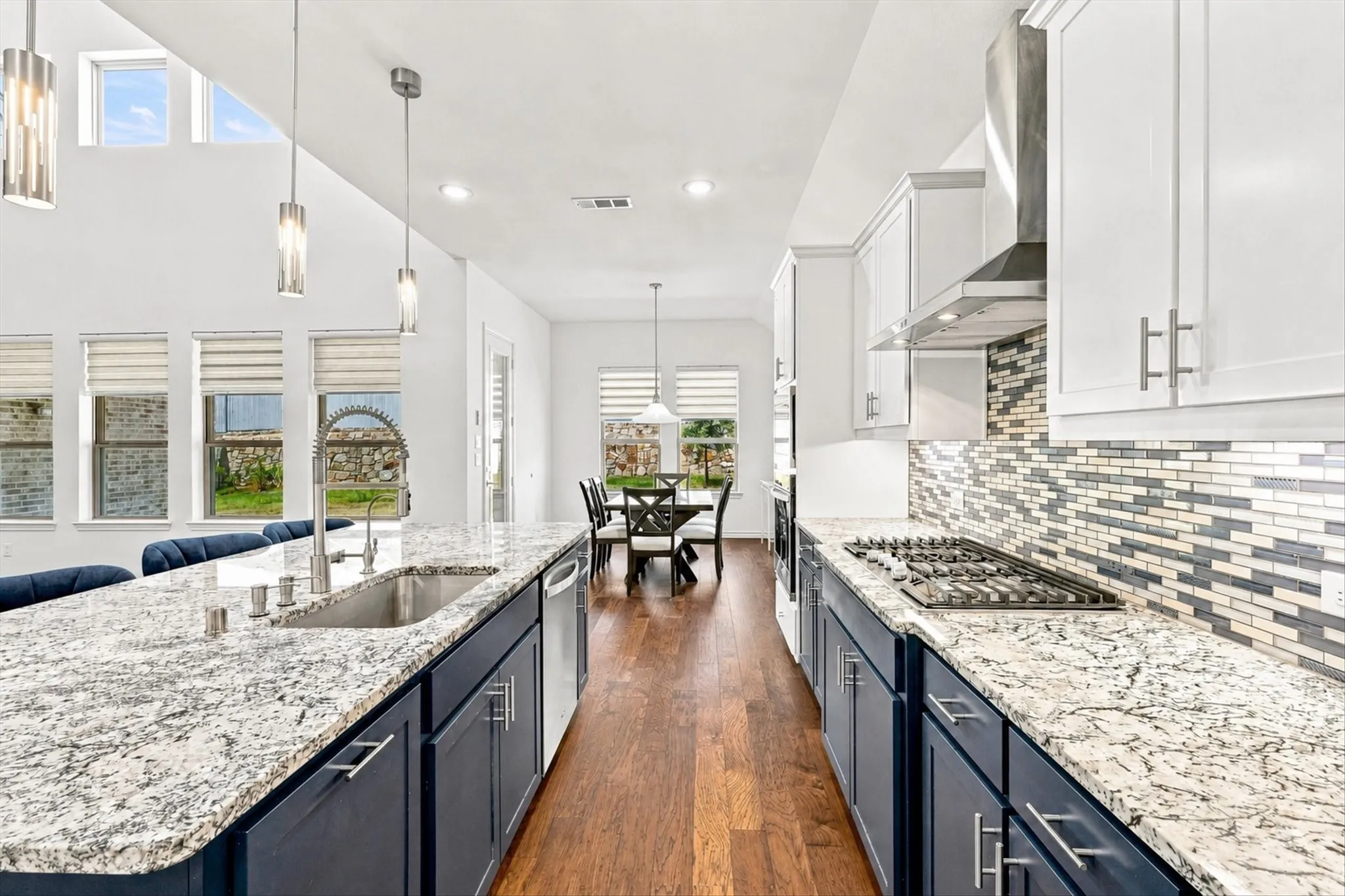 Kitchen featuring a gas cooktop, stainless steel range hood, mosaic tile backsplash, wood-finish flooring, and pendant lighting