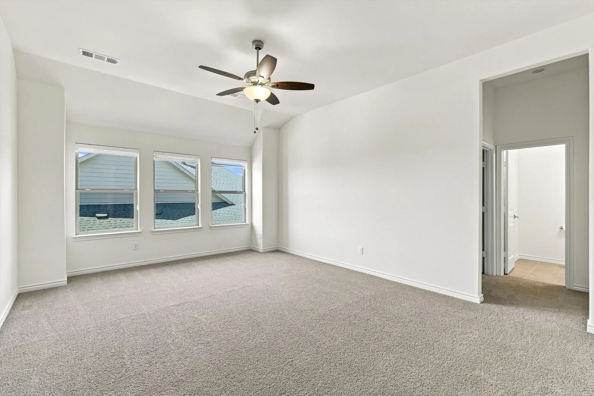 Vaulted ceiling, ceiling fan with integrated lighting, three large windows, neutral carpet, and white walls