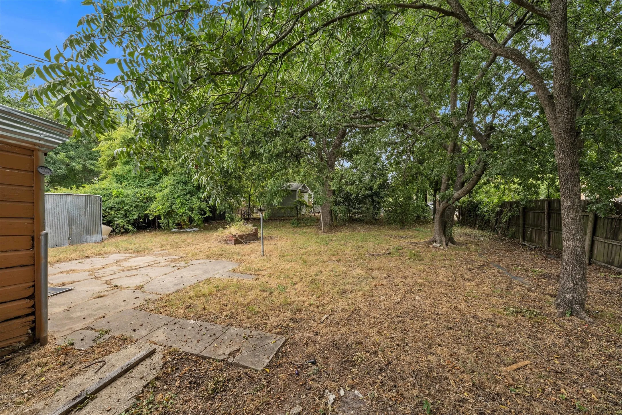 Expansive backyard featuring mature trees, a wood privacy fence, and a concrete patio area