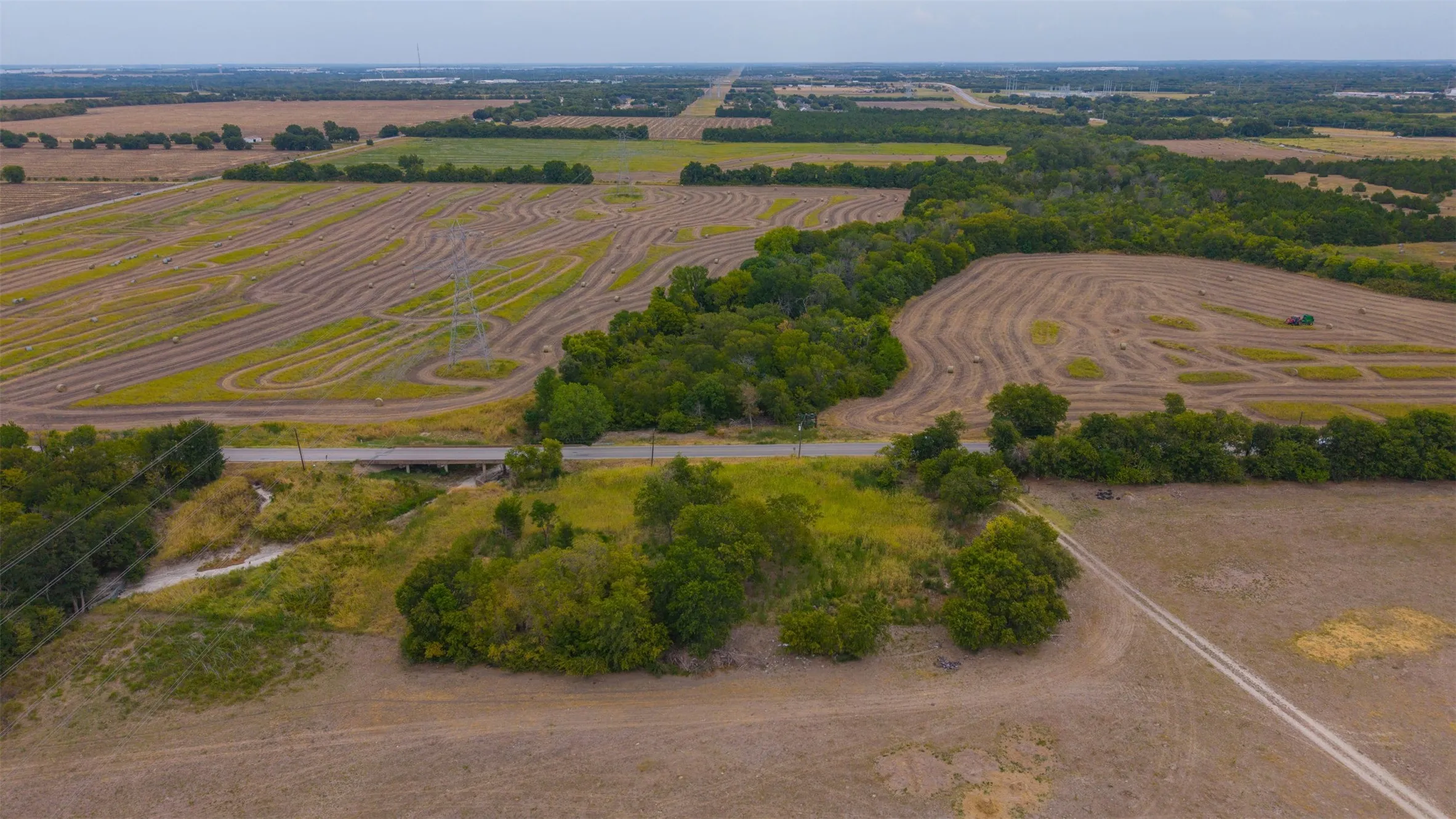 Expansive agricultural land featuring cultivated fields, mature tree lines, and a paved road with a bridge