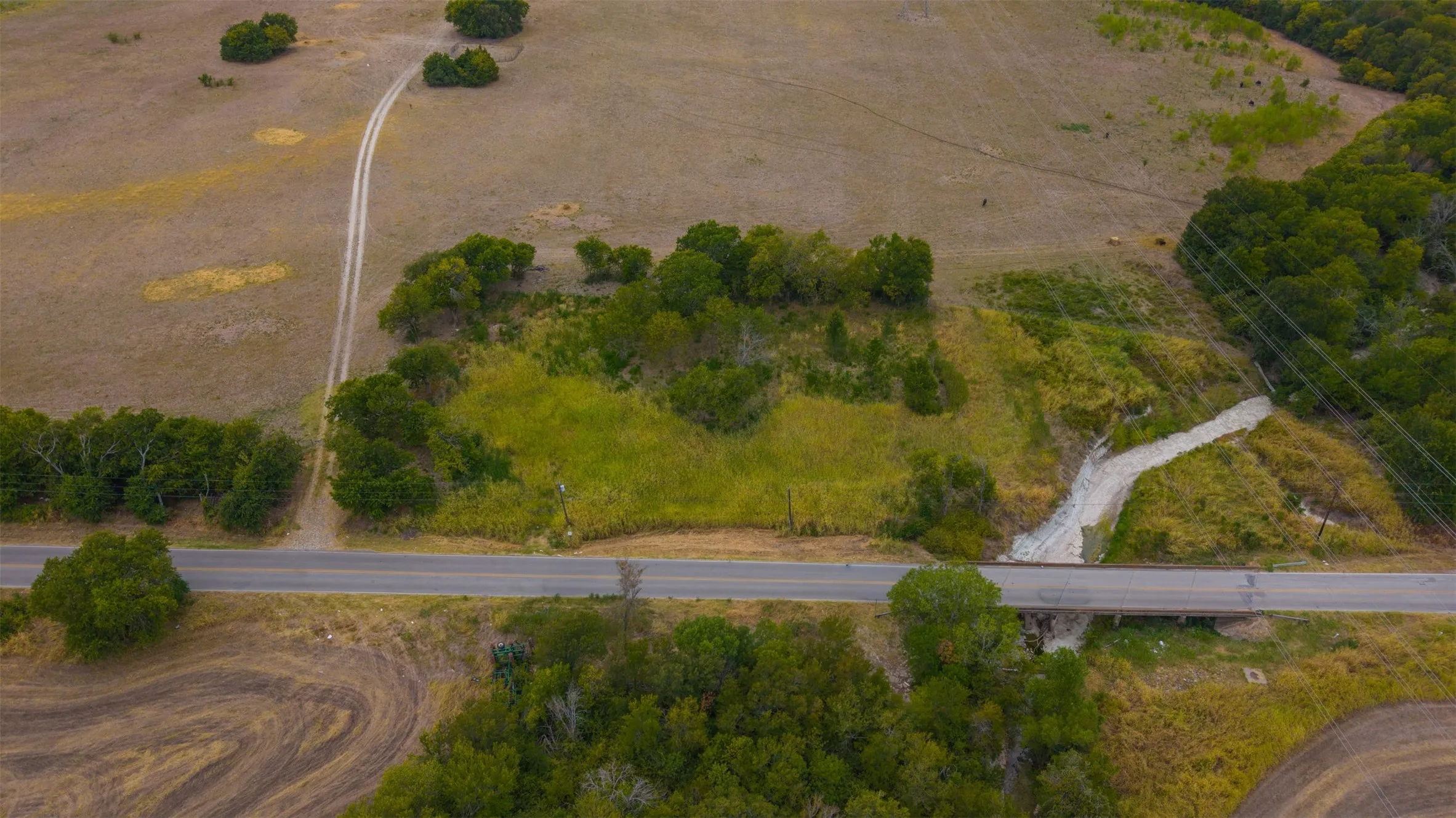 Expansive land parcel featuring a paved road, a bridge structure, mature trees, and an unpaved access path