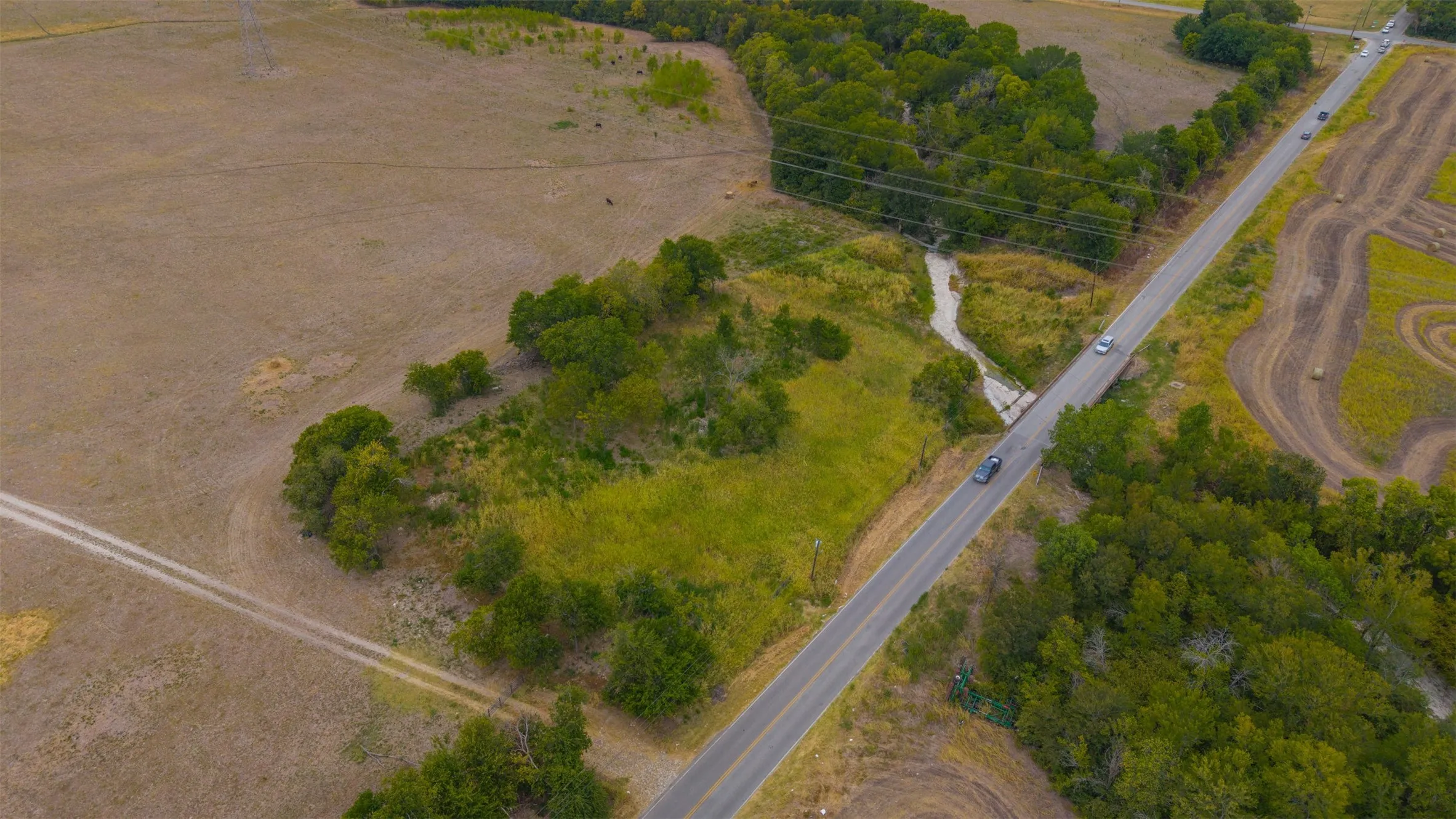 Expansive undeveloped land featuring a paved road frontage, natural stream, and mature trees
