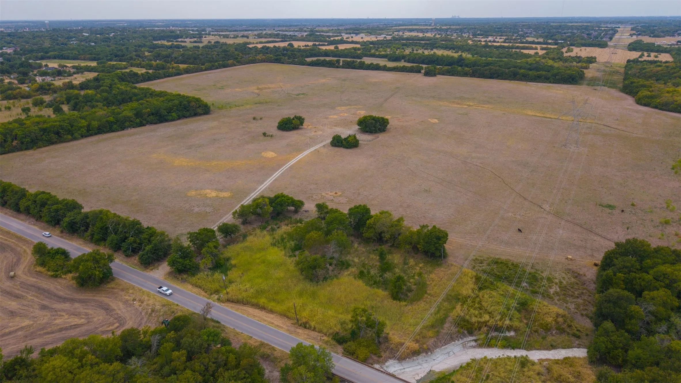 Expansive rural landscape featuring open fields, scattered trees, and a bordering paved road