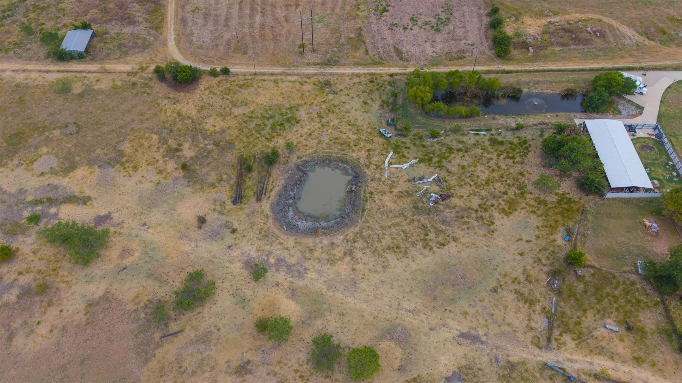 Expansive property featuring an open field, a natural pond, and a large outbuilding with a metal roof