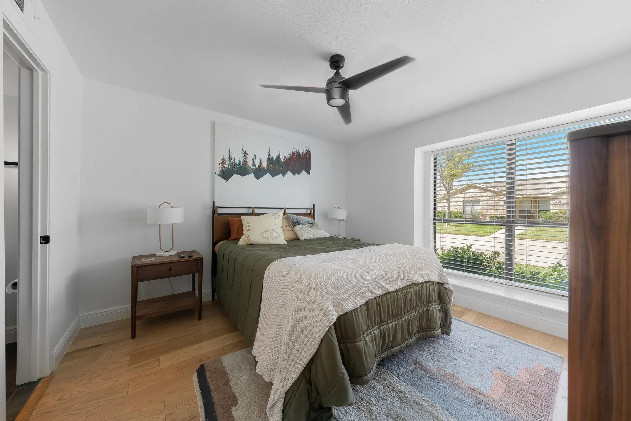 Expansive window with blinds, modern ceiling fan, light wood-finish flooring, and white walls
